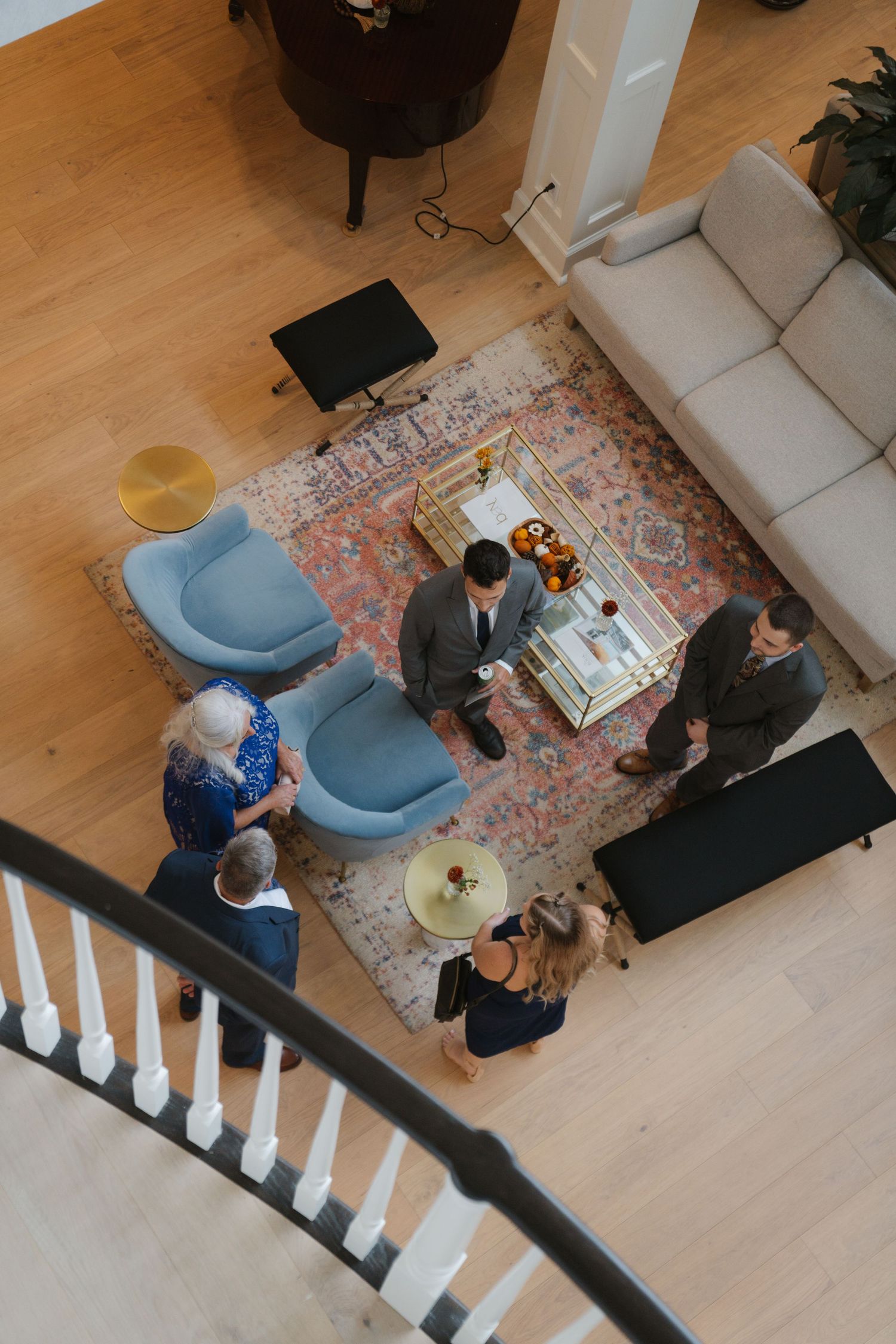 Overhead view of people gathered in a modern living room with hardwood floors and a curved white staircase railing.