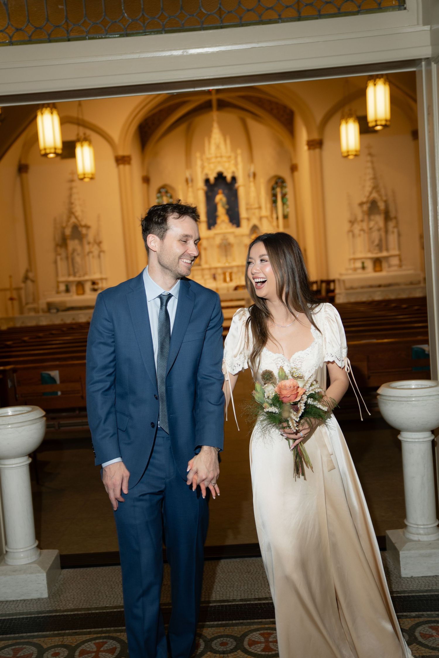 A couple shares a joyful moment together in a church with warm lighting and gothic architecture.