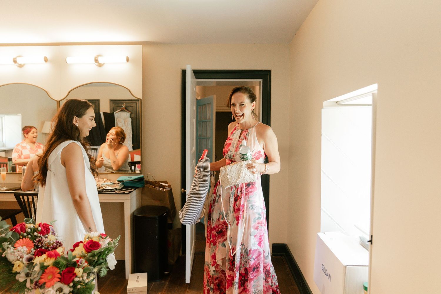 A bride and bridesmaids in floral robes prepare for a wedding day in a bright, sunlit room.