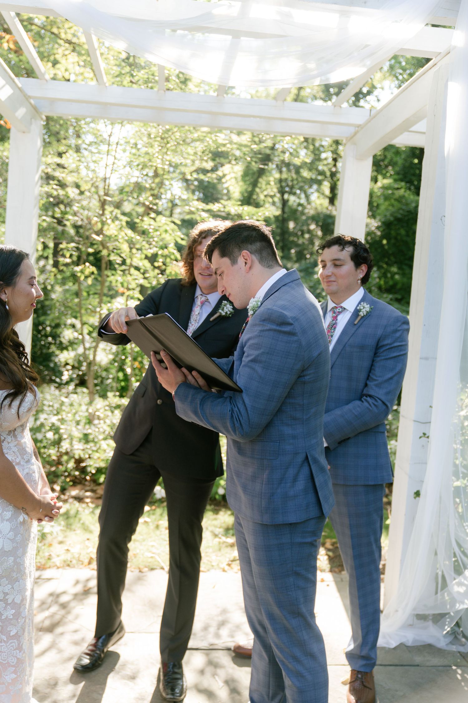 Wedding party members share emotional reactions during a ceremony under a white gazebo.