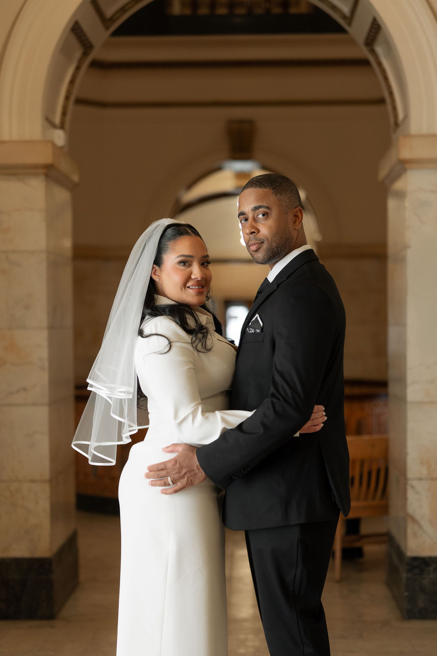 A bride and groom pose together under an elegant stone archway.