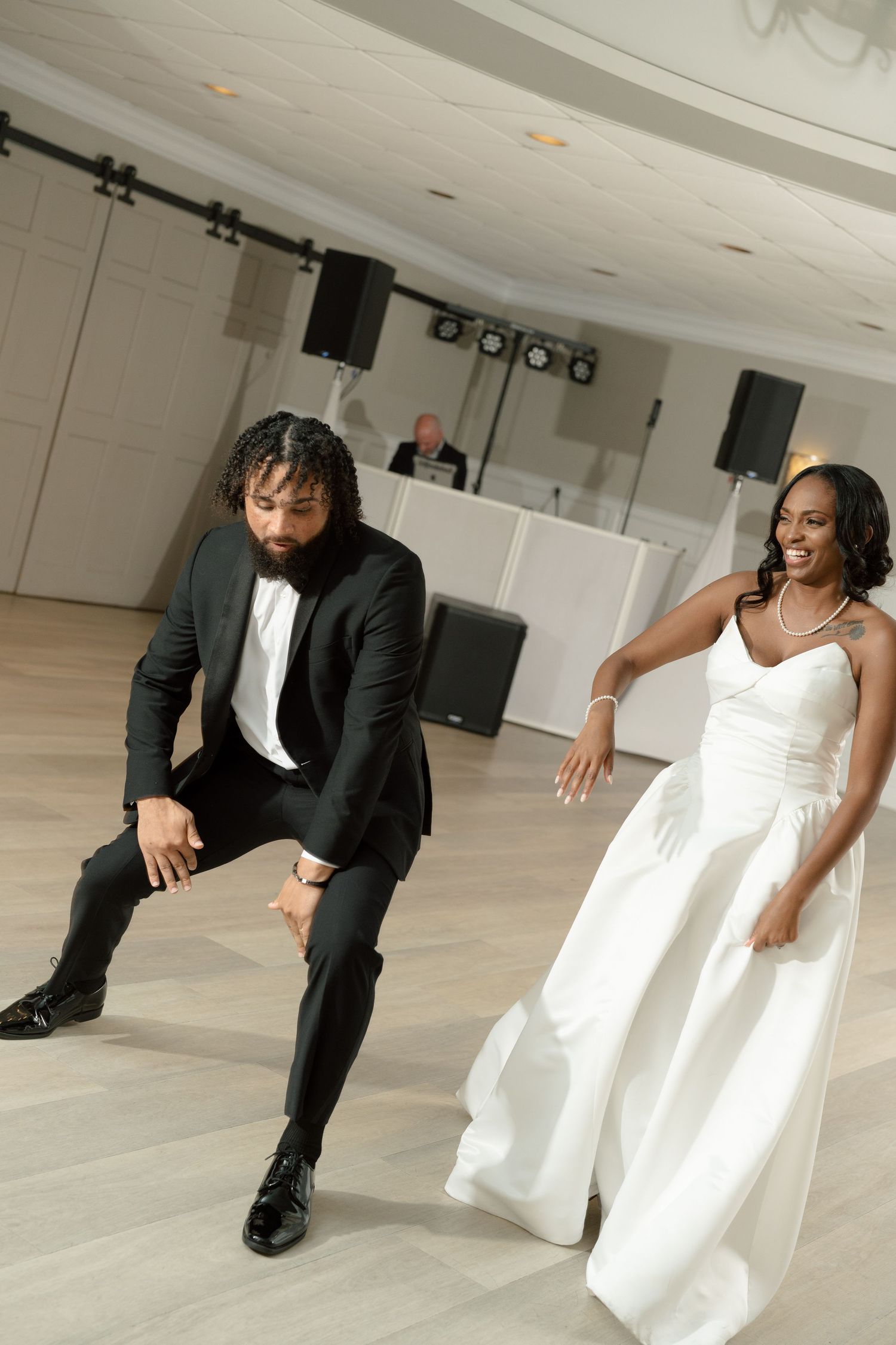 Bride and groom perform energetic first dance routine on white dance floor at wedding reception.