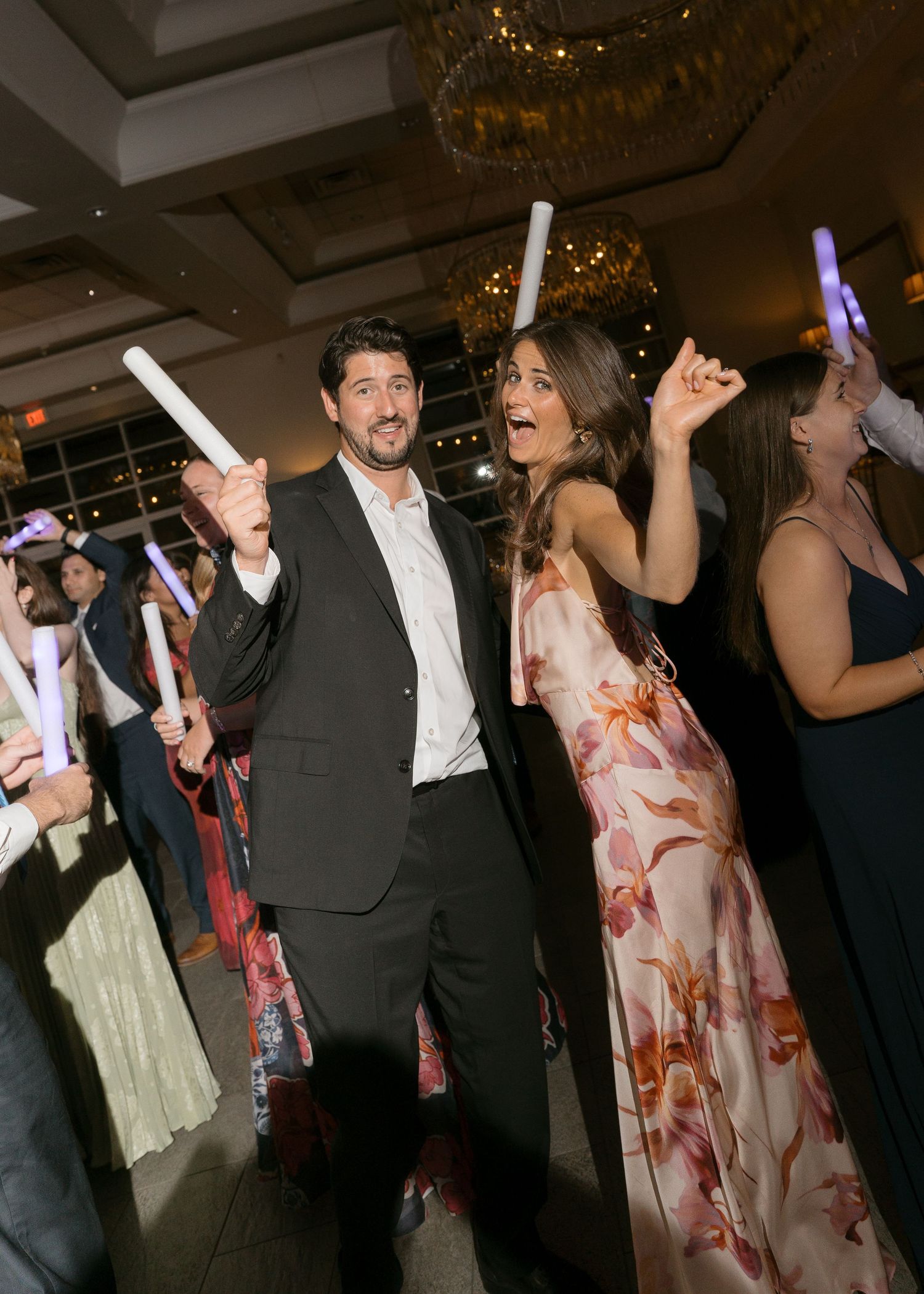 Wedding guests celebrate on the dance floor waving glowing foam sticks during the reception party.
