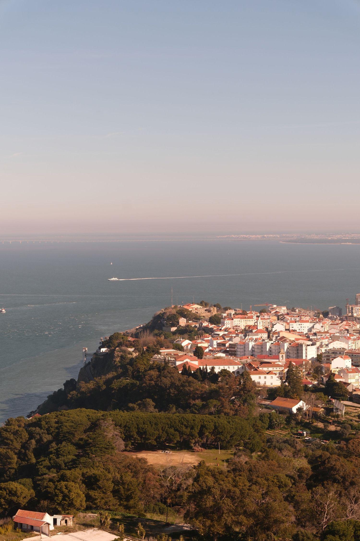 Panoramic coastal view of white buildings nestled on hillside overlooking the ocean during sunset.