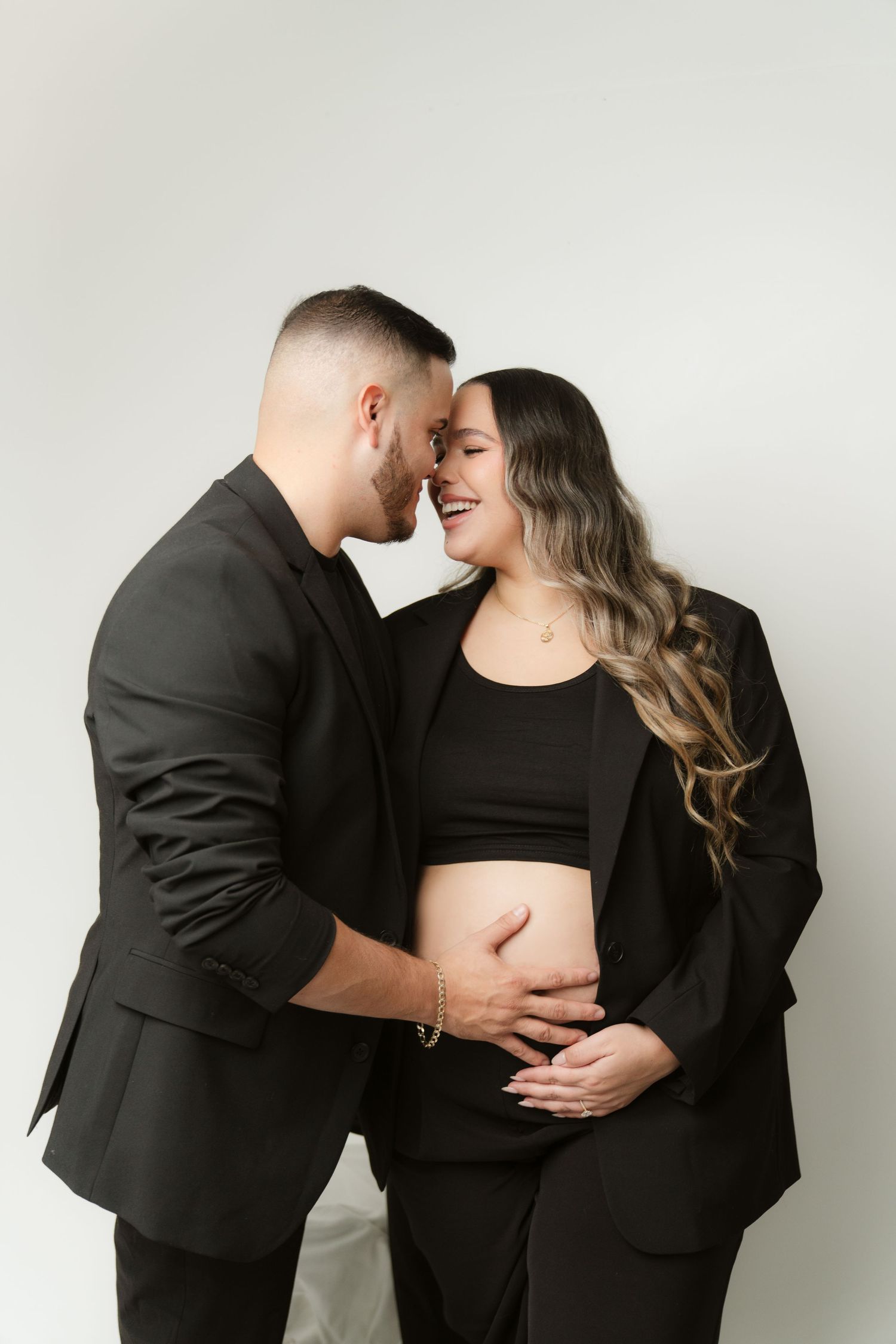 Intimate maternity photoshoot with couple wearing black against white background.
