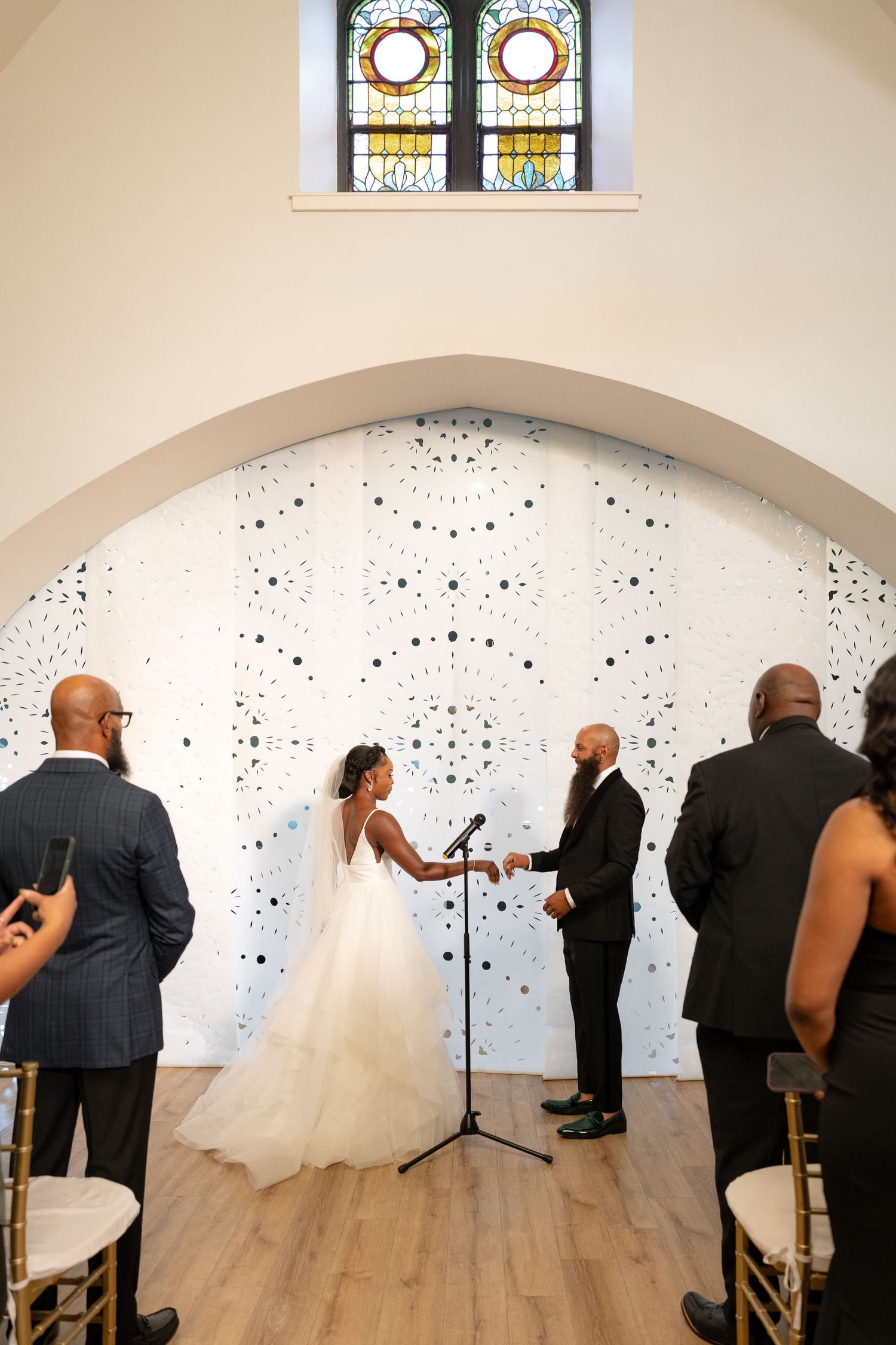 Wedding ceremony sequence showing interactions in front of stained glass windows and patterned walls.