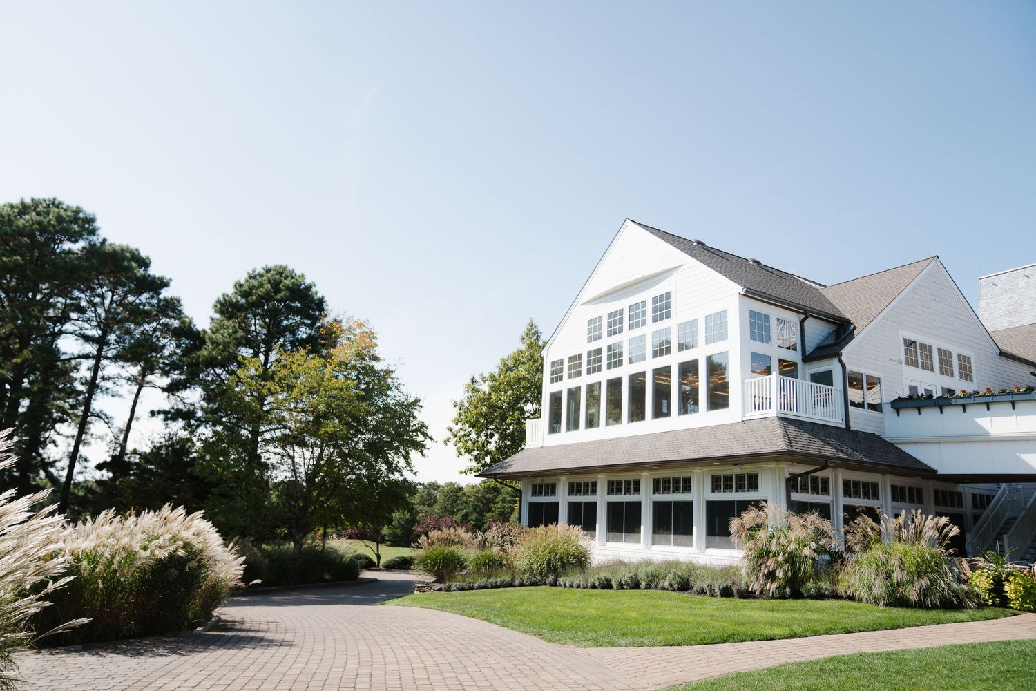 A series of modern white coastal homes with large windows and architectural details set against a blue sky and trees.