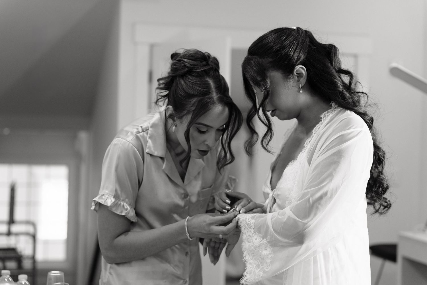 Two women in robes share an emotional moment looking at a phone during bridal preparations in black and white.