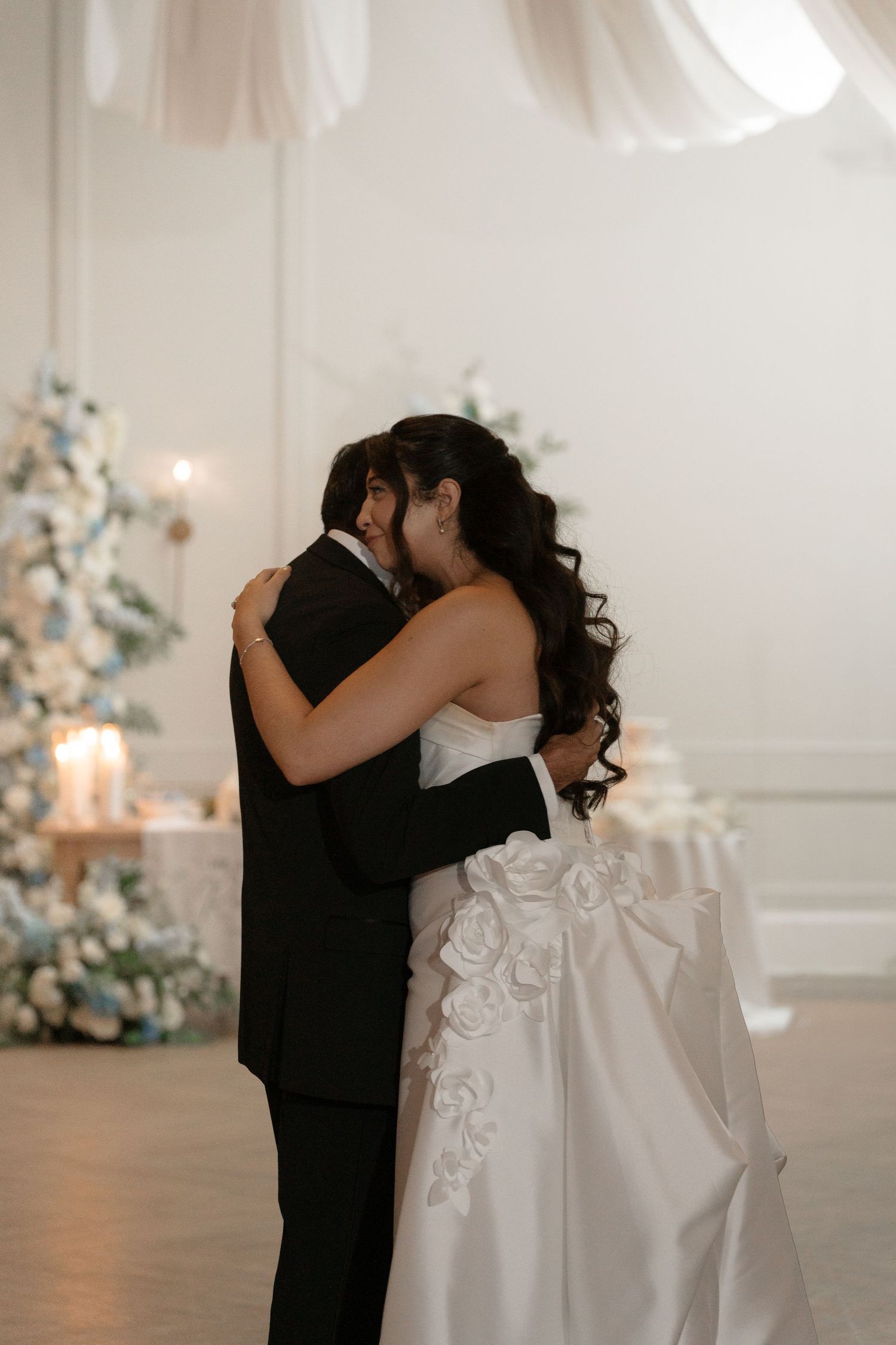 Bride and groom share intimate embrace during first dance near candles and white floral arrangement.