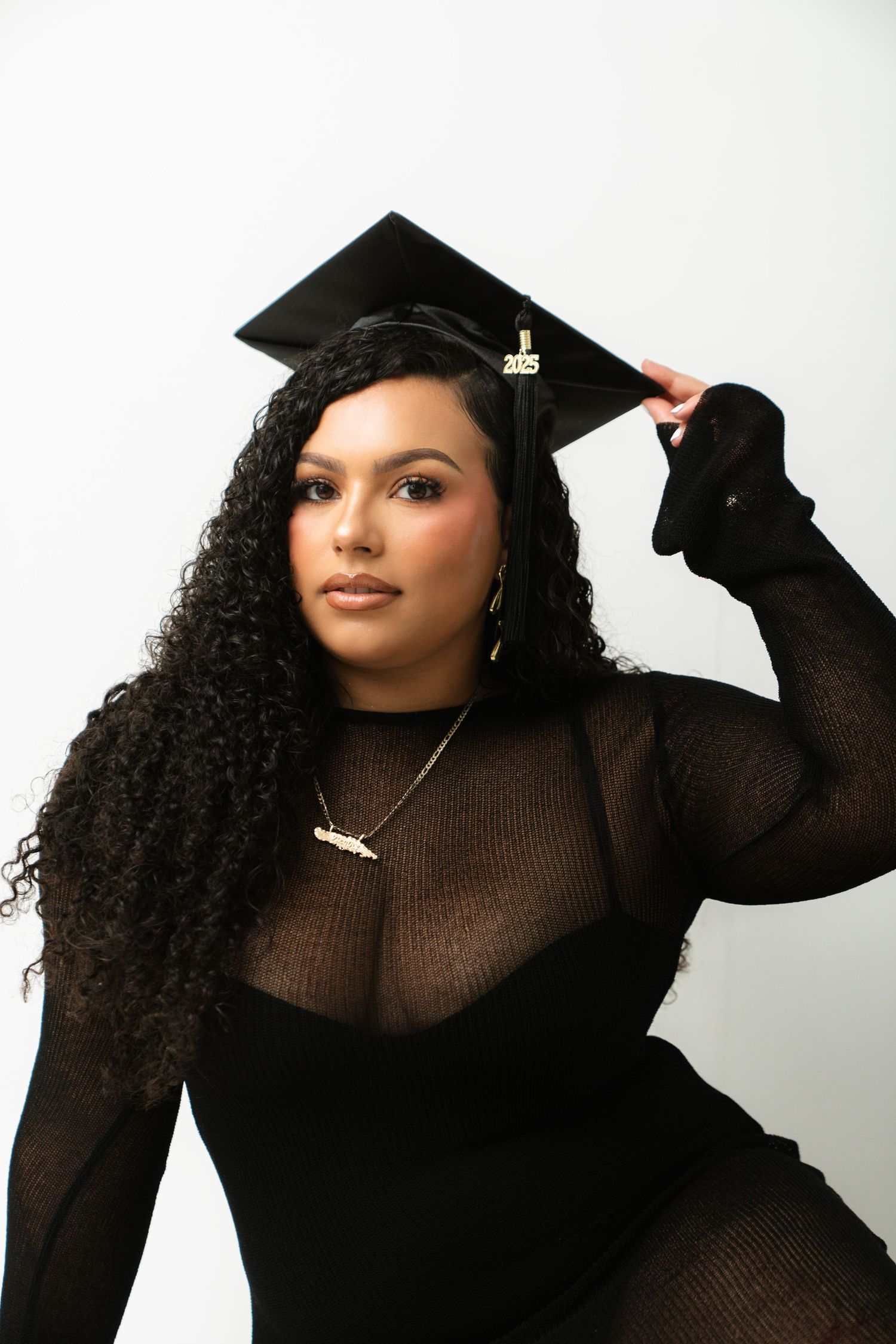 Graduate in a black sweater poses with their diploma and graduation cap against a white background.