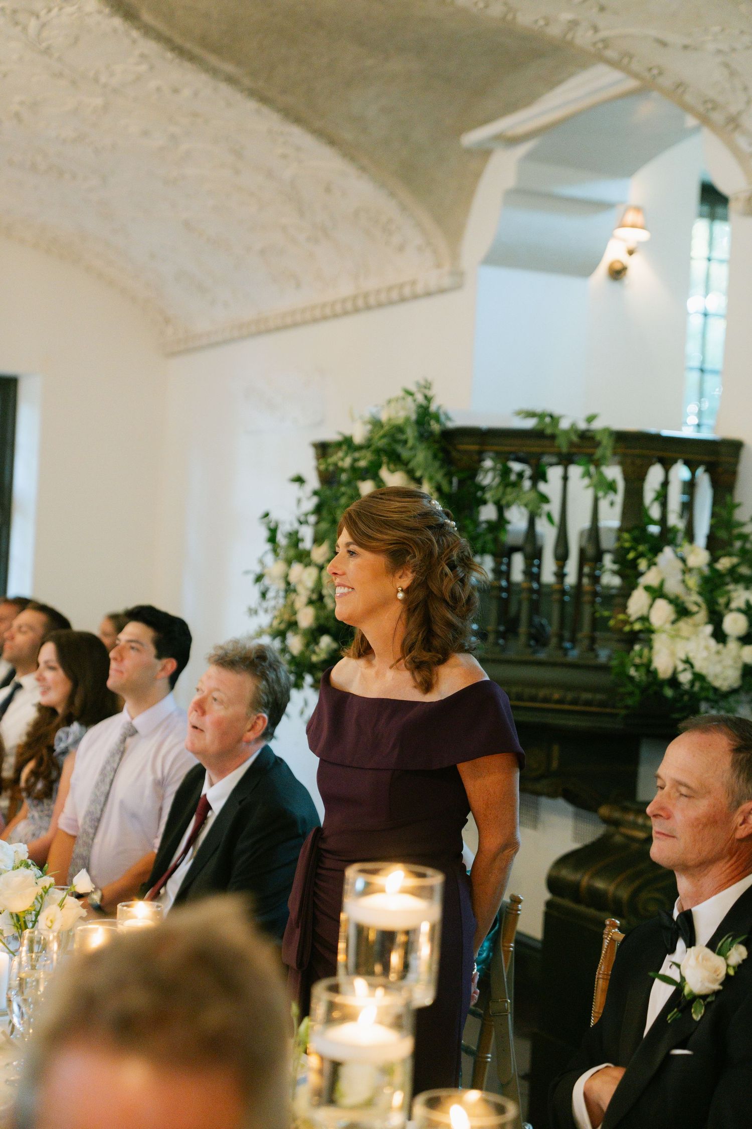 Wedding reception guests seated at elegant tables with candlelight in a historic venue.