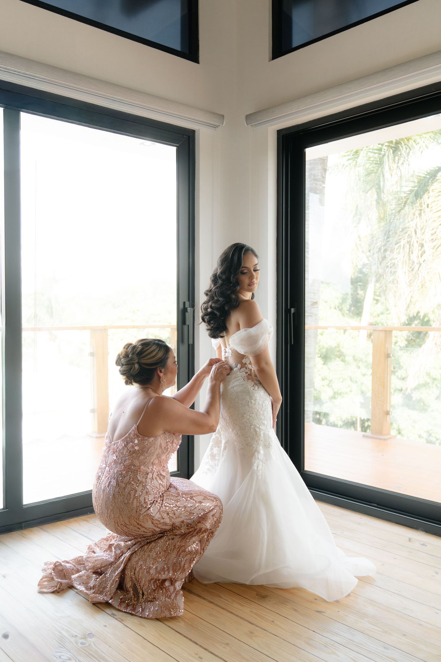 Wedding dress being adjusted in a bright sunlit room with large windows.