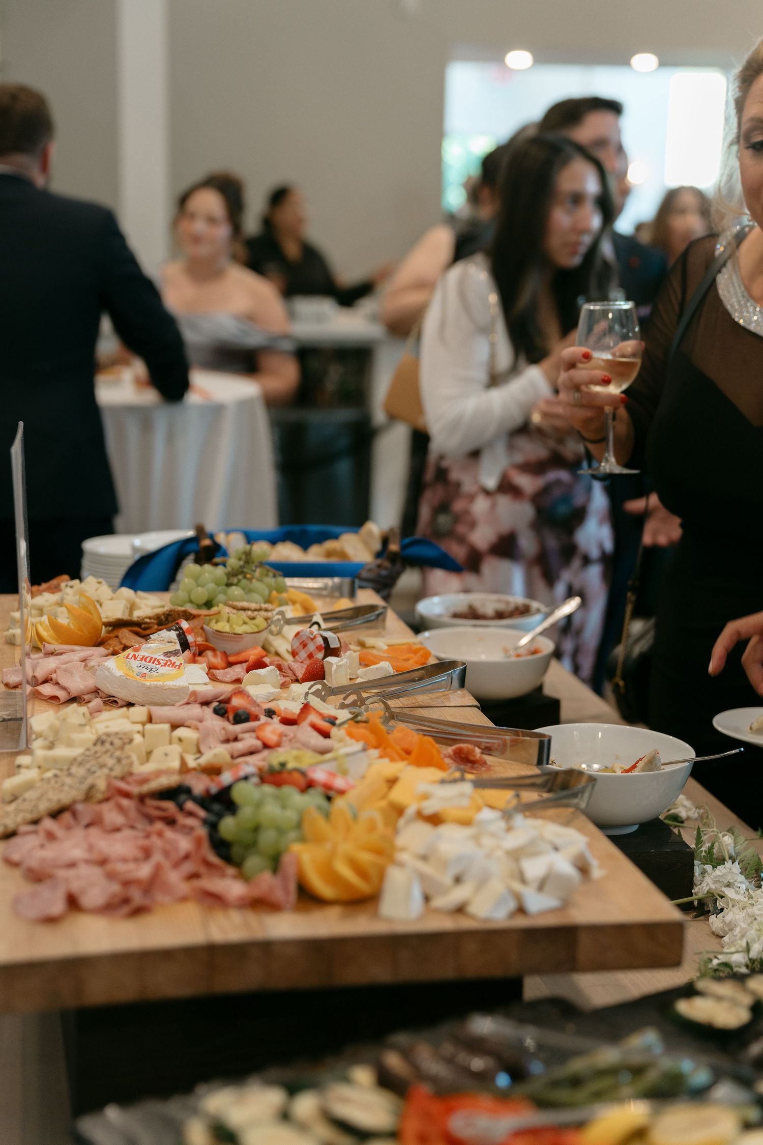 Guests mingle near a charcuterie board with meats, cheeses, and fruits at a wedding reception.