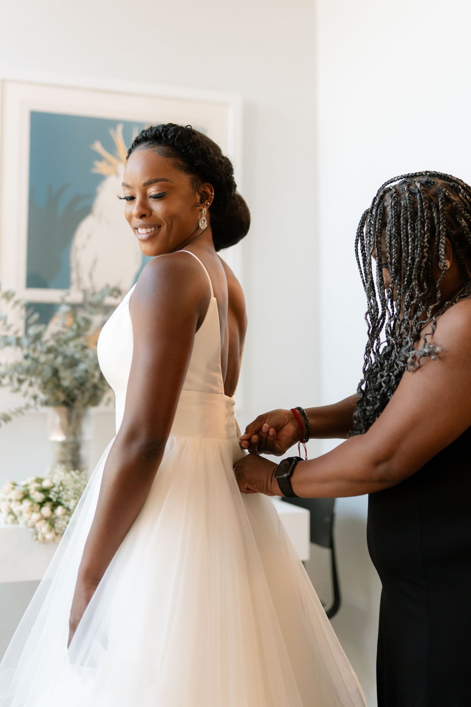 Elegant bride in white V-neck gown getting final dress adjustments before ceremony.