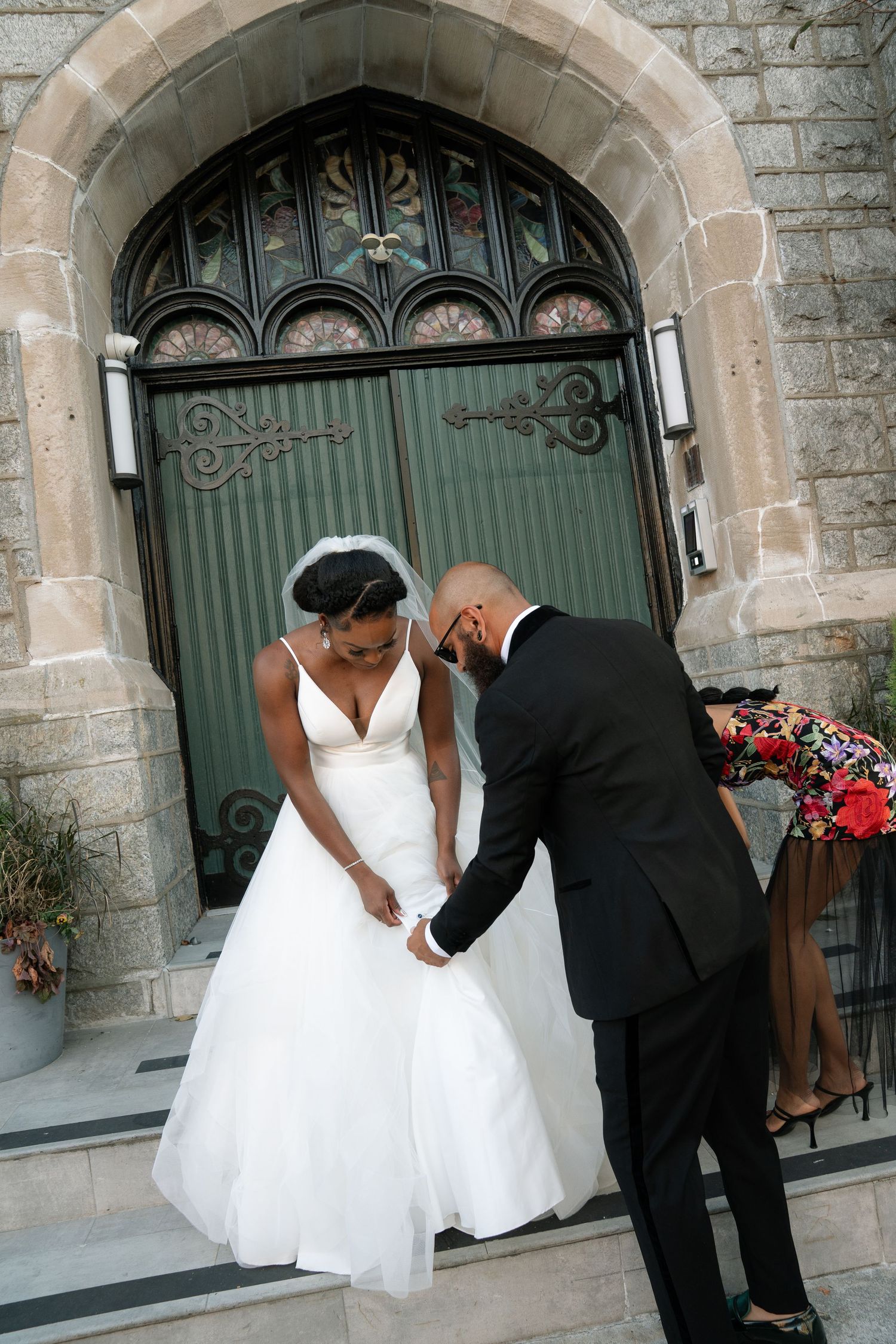 Couple holds hands on church steps in front of ornate gothic doorway.