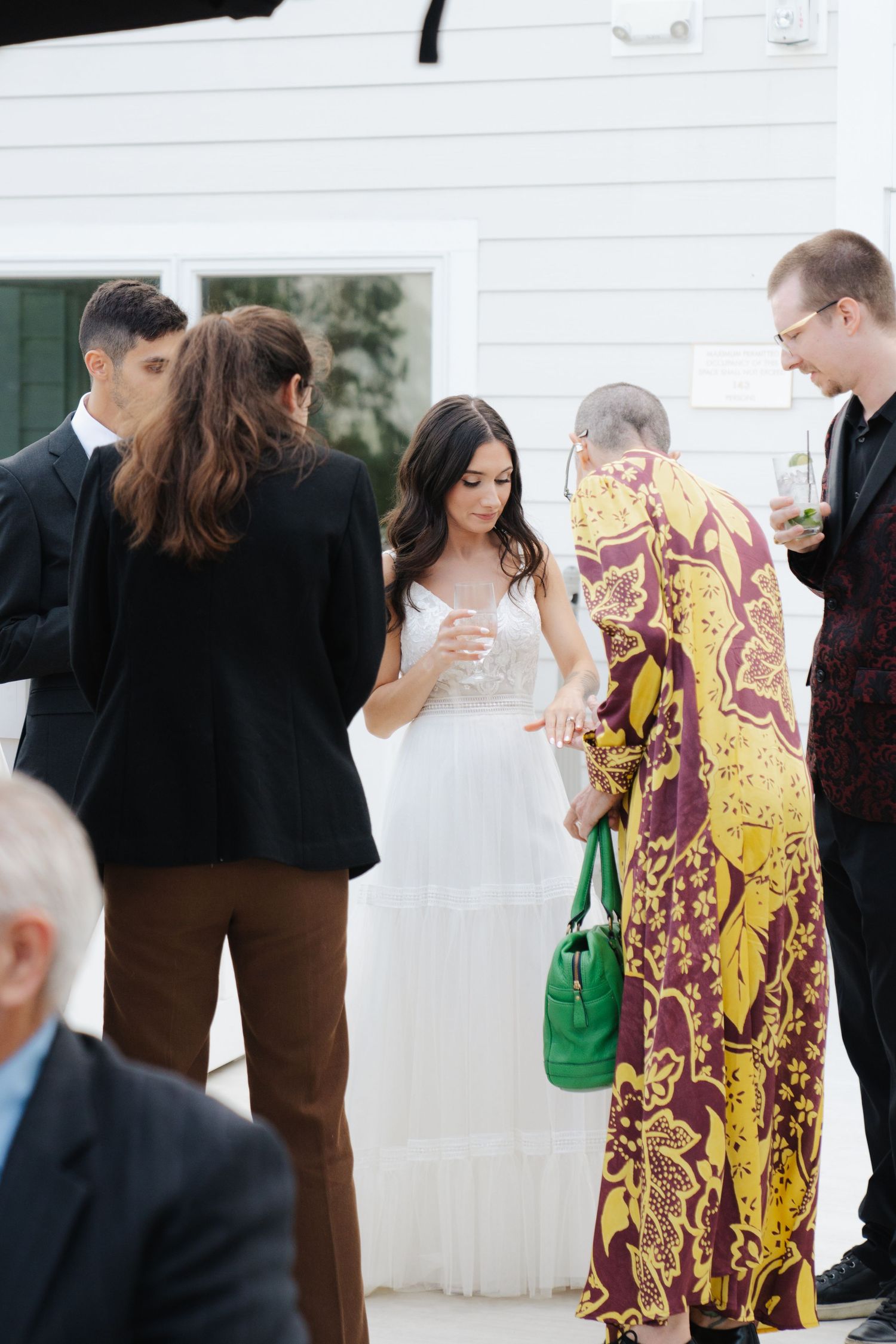 Wedding guests gather outdoors in formal attire with a person wearing a distinctive yellow and burgundy patterned dress.