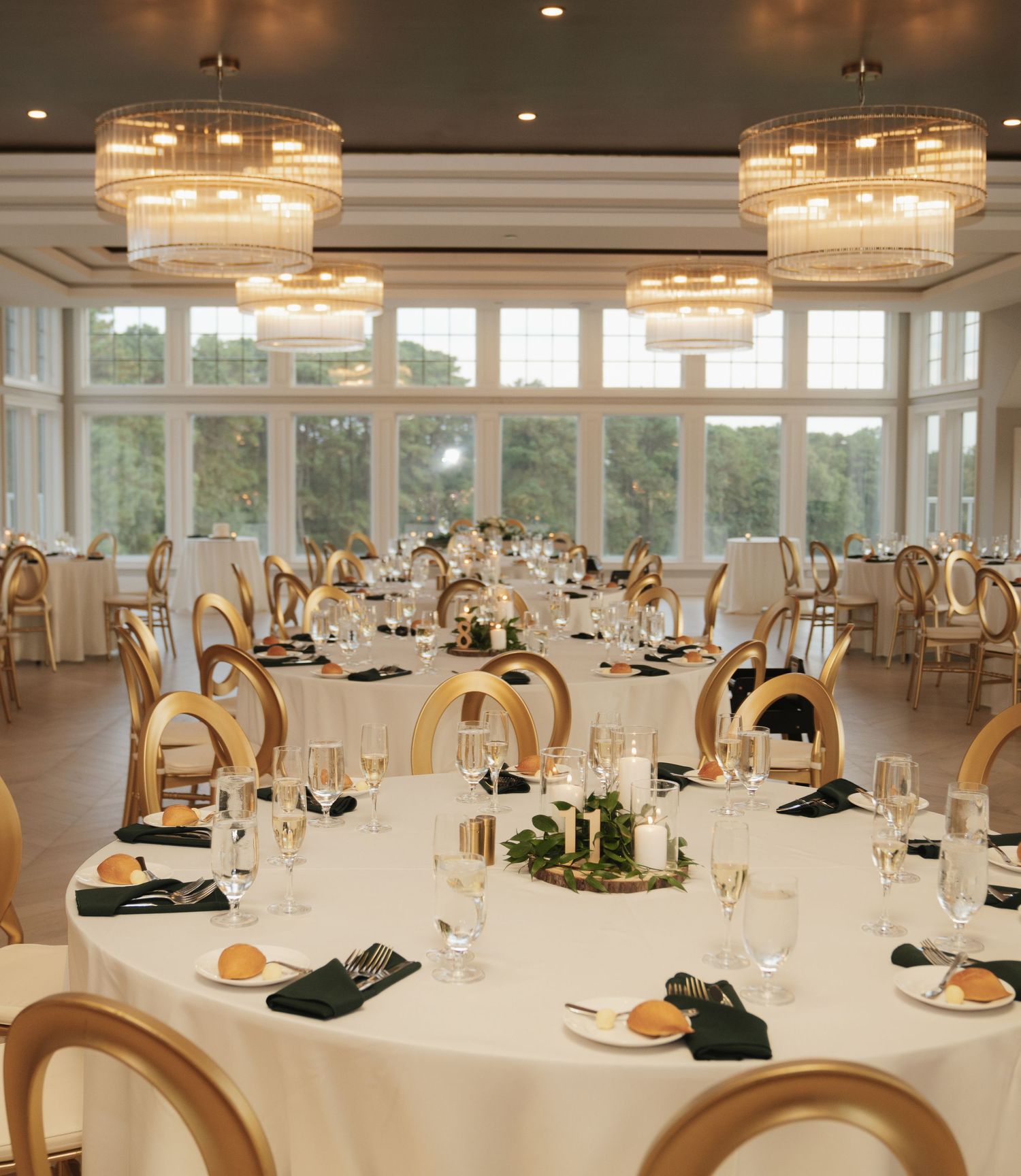 Elegant wedding reception venue with round tables, gold chairs, crystal chandeliers and dark green napkins.