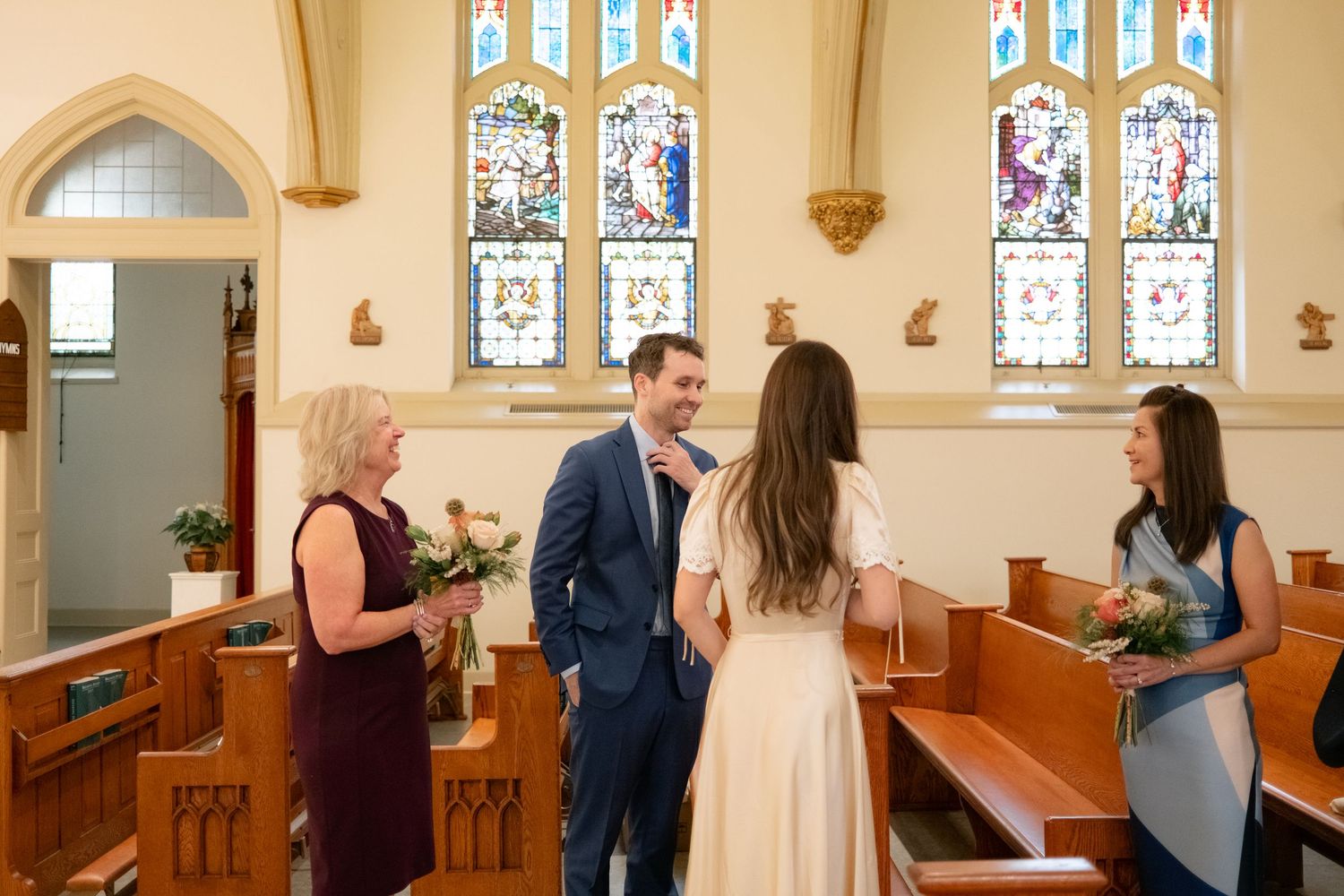 A couple stands together in a beautiful church interior with stained glass windows and ornate architecture.