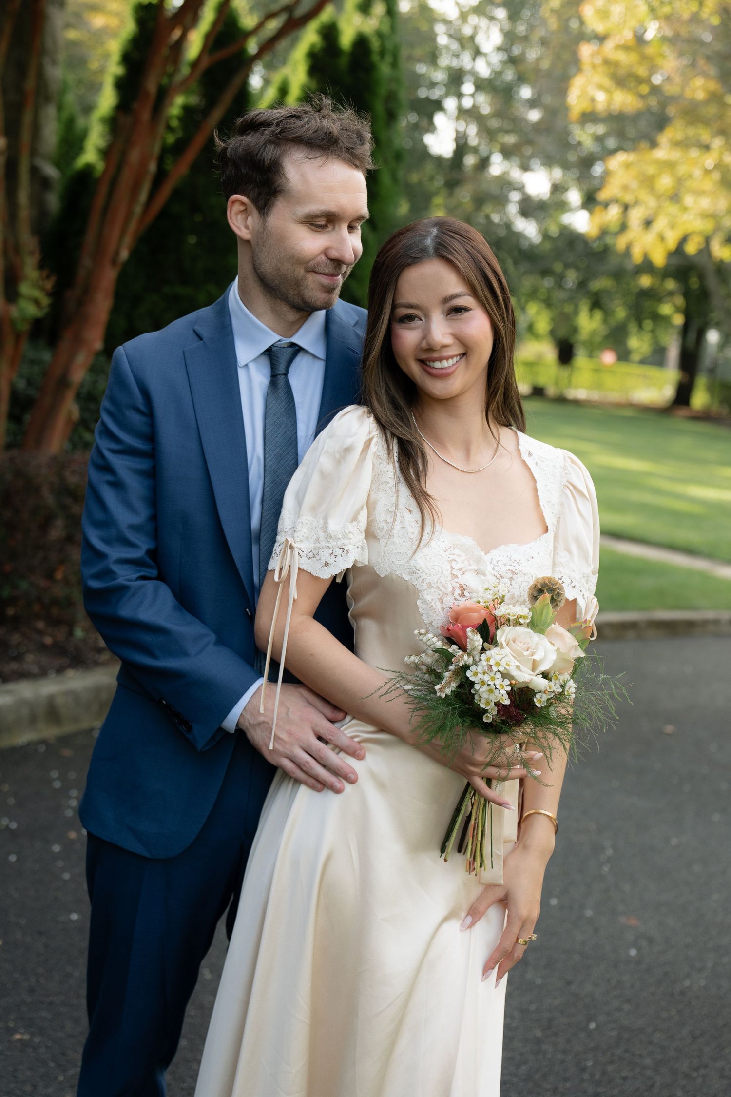 A romantic wedding photo series showing a couple in a park with autumn trees, wearing a navy suit and cream dress.