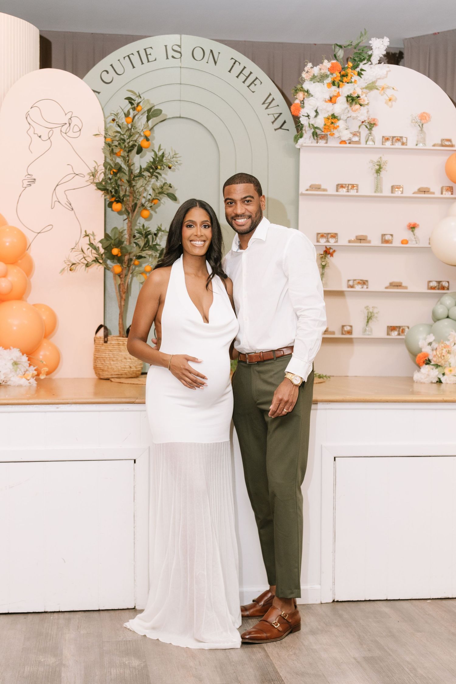 An elegant indoor photoshoot with white and olive green outfits against a decorated wall with shelving.