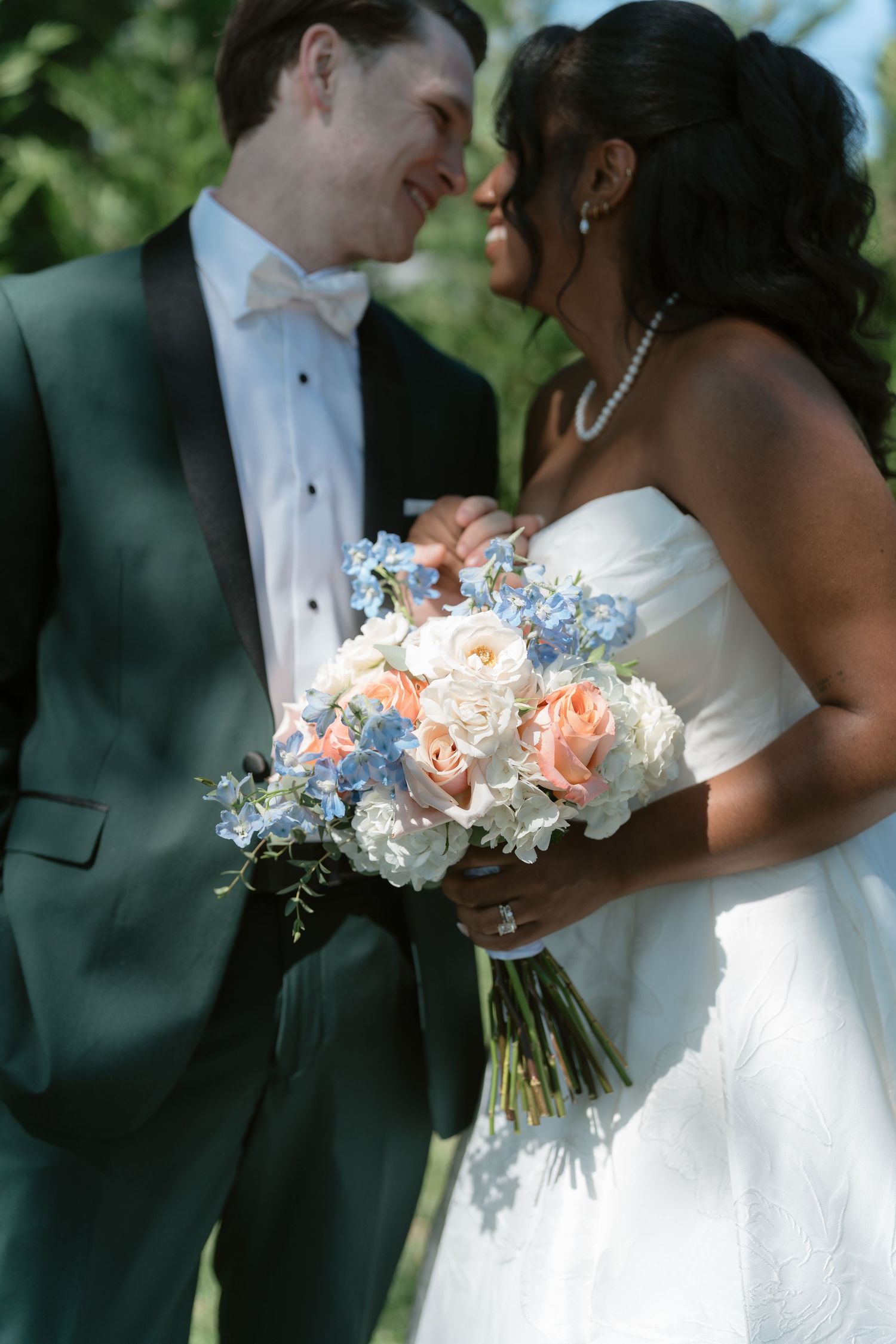 Interracial couple shares romantic moment holding a bridal bouquet of pink roses and blue flowers.