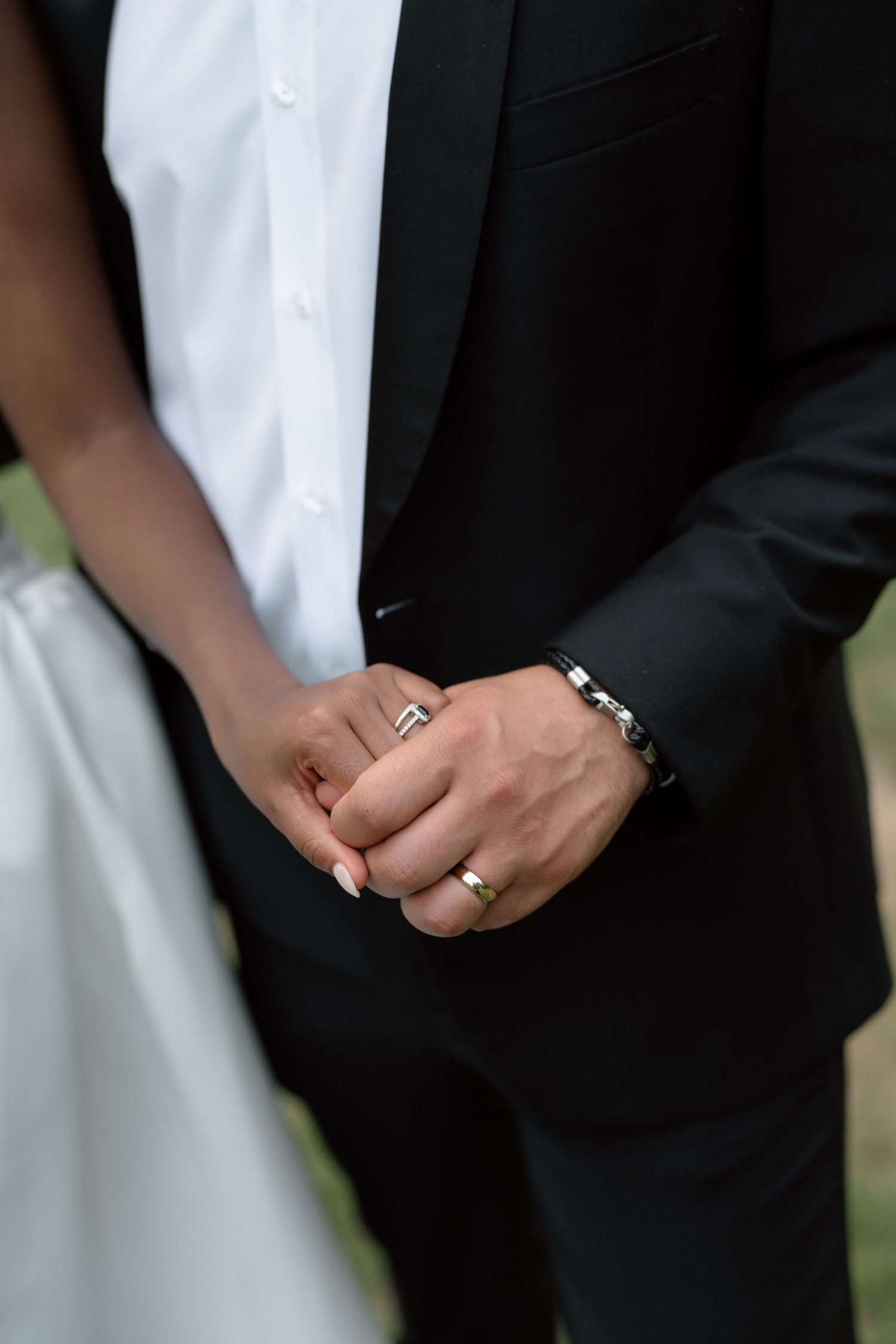 Close-up of newlyweds holding hands displaying wedding rings and bracelet after ceremony.