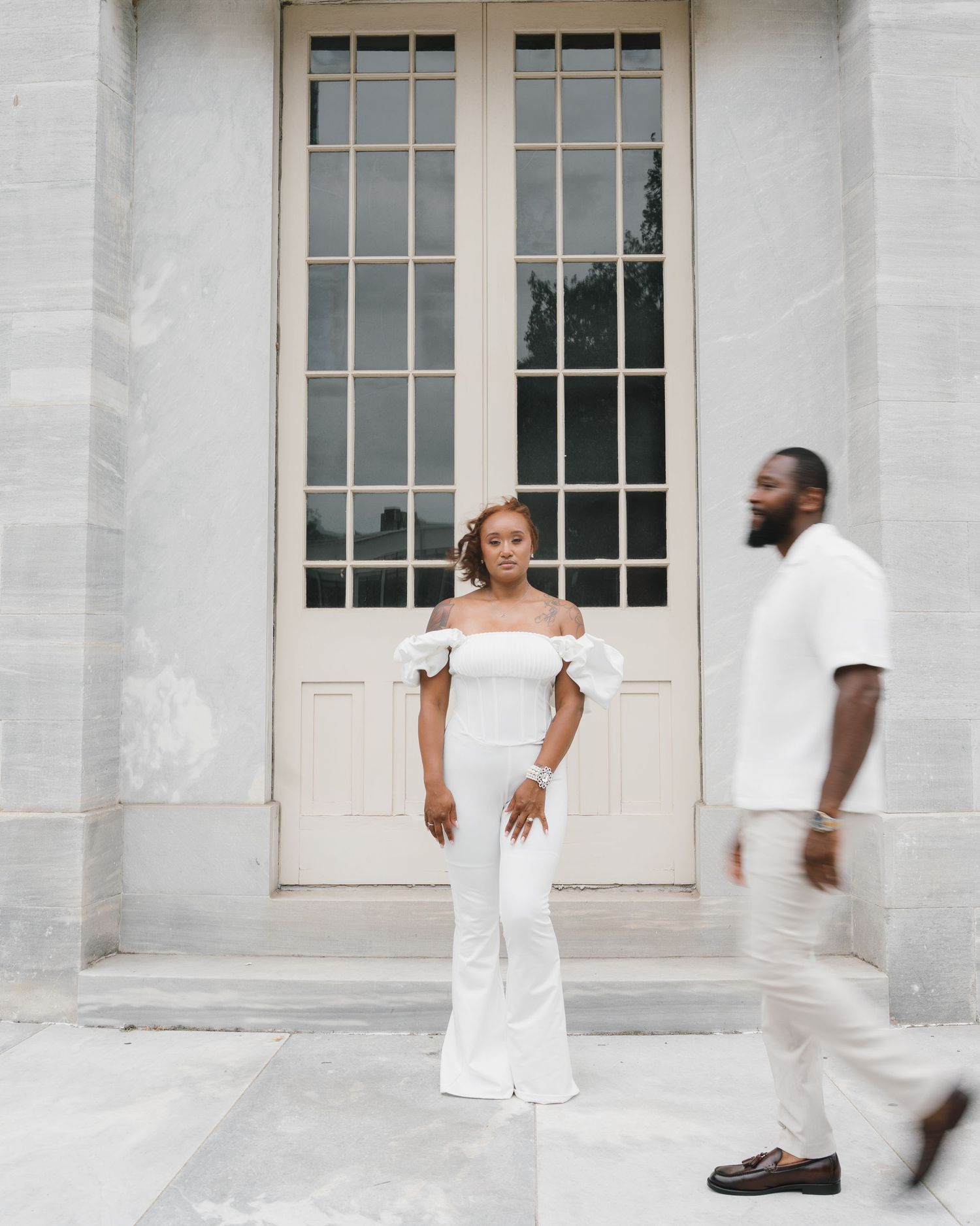 Artistic motion blur photograph of dancers in white clothing against a classical white stone building facade.