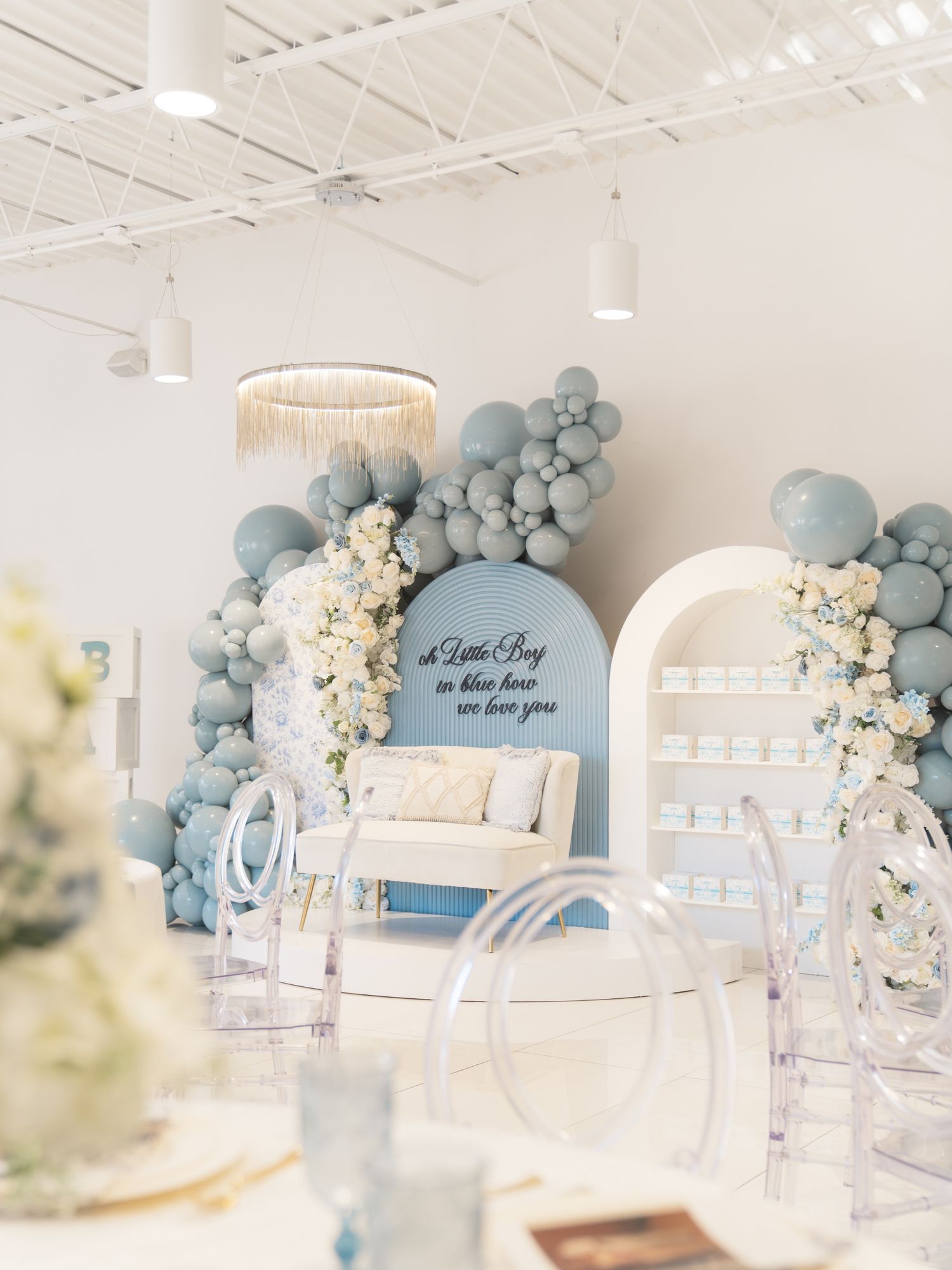 An elegant event setup with blue and white balloon arch and floral decorations.