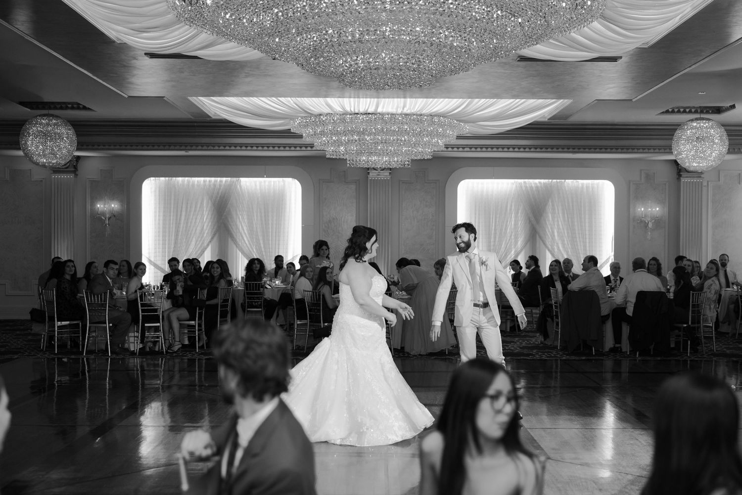 A large elegant ballroom with crystal chandeliers and people dancing during a wedding reception.