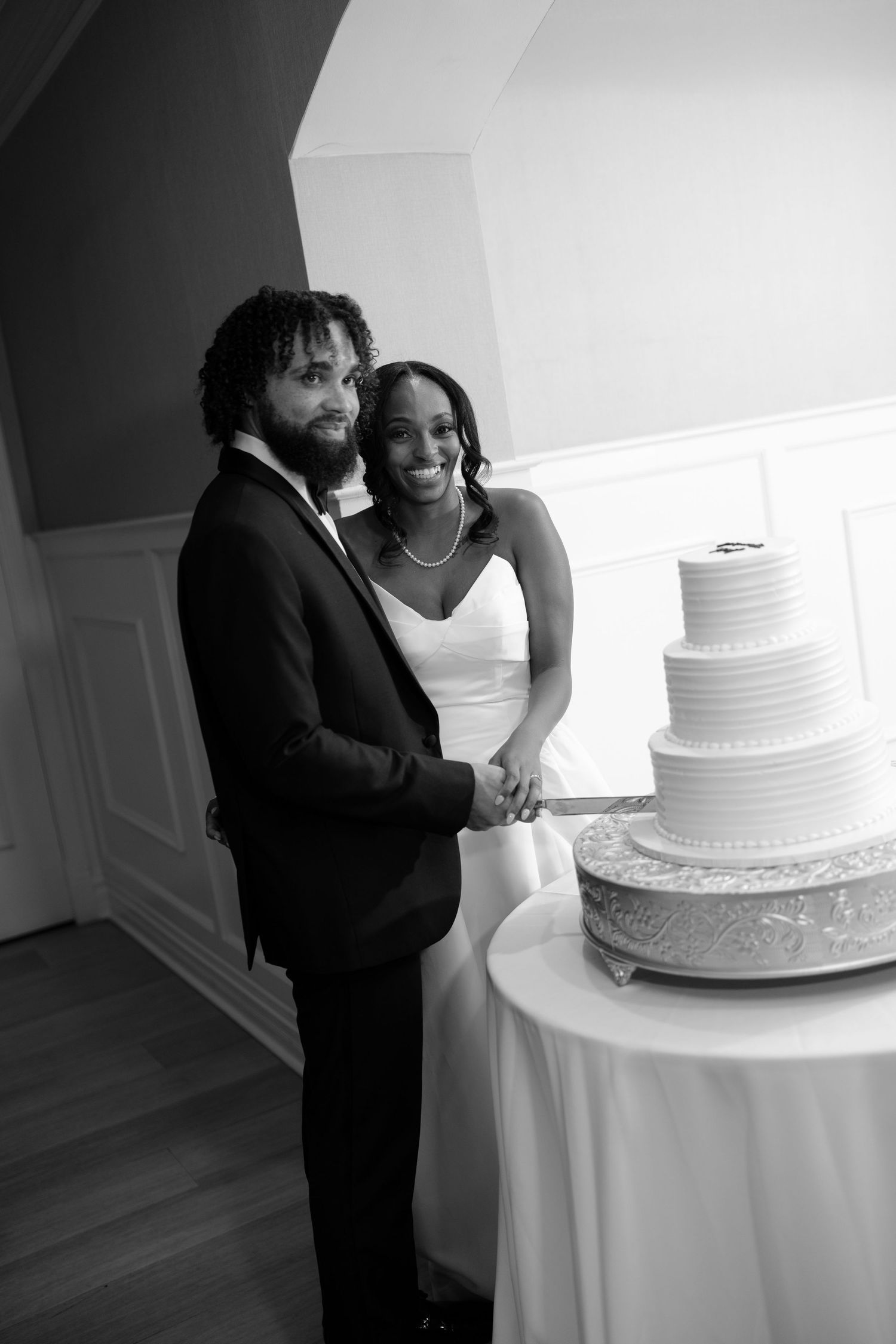 Bride and groom cut their elegant four-tier white wedding cake in a black and white portrait photo.
