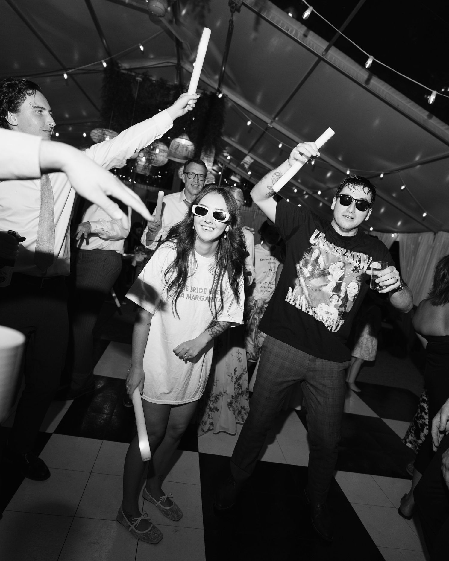 Black and white photo of wedding guests dancing with sunglasses at a lively reception party.