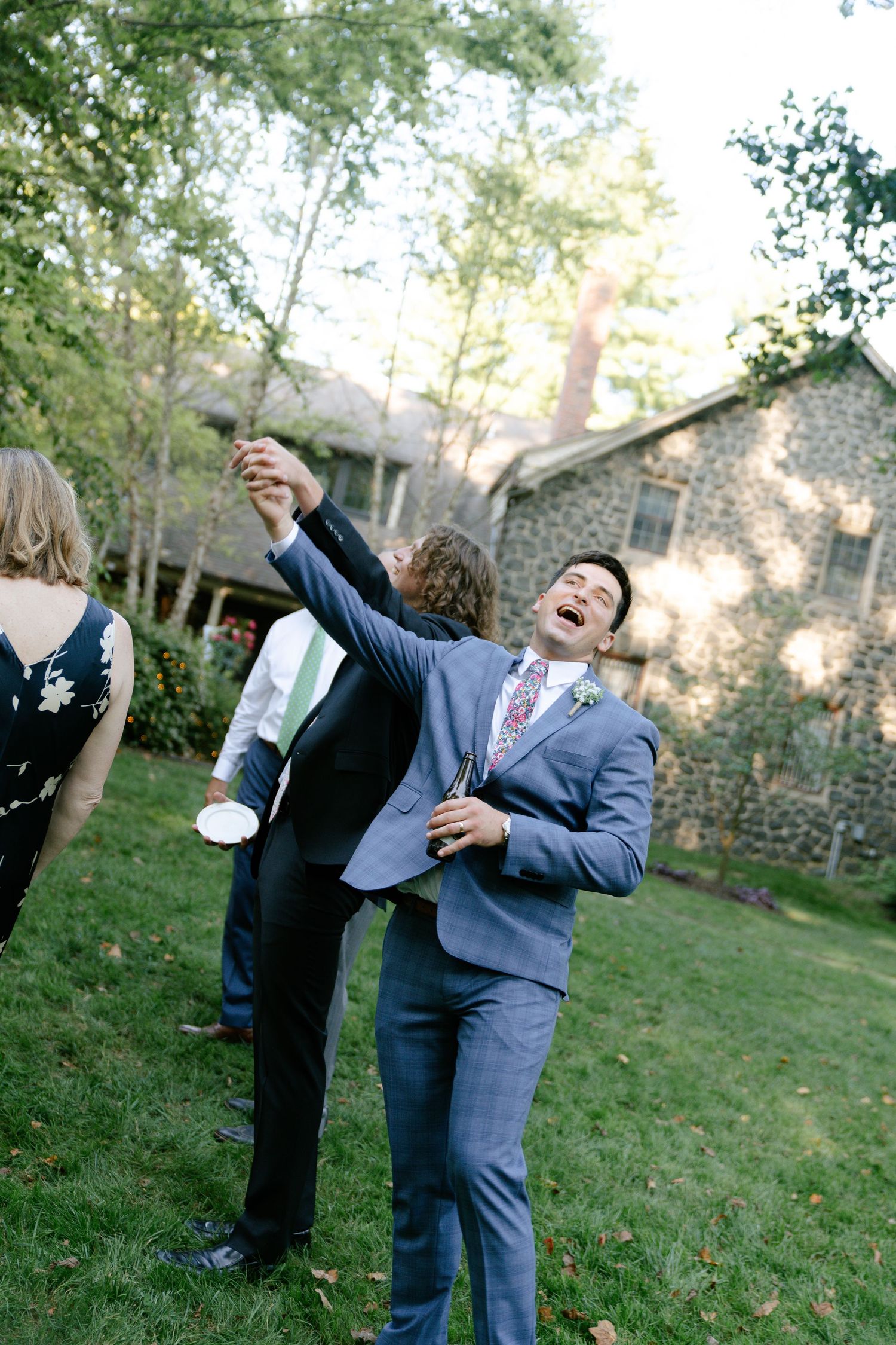 Wedding guests dance and celebrate joyfully on an outdoor lawn.