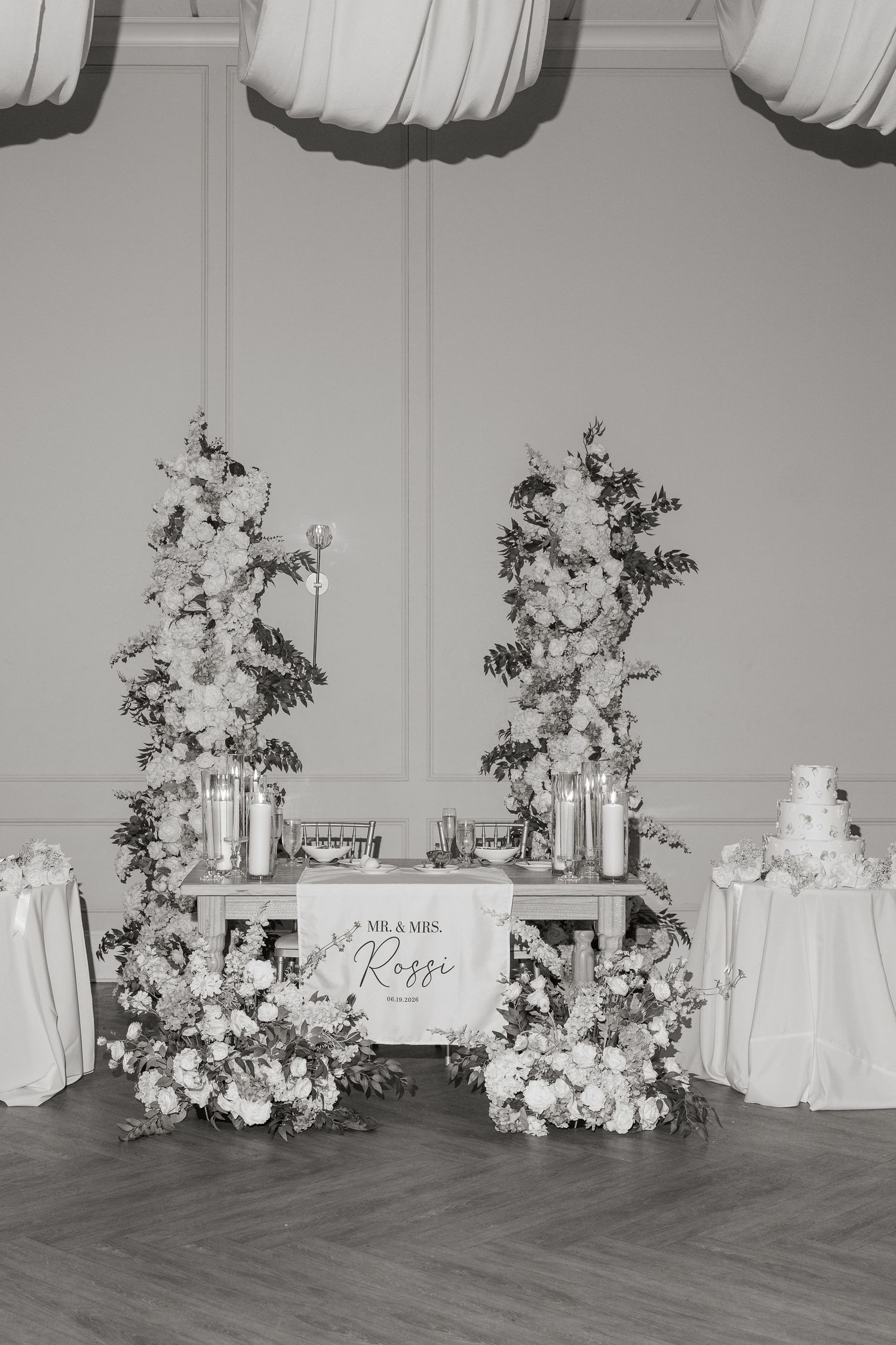 Black and white image of elegant Mr. and Mrs. Rossi sweetheart table with floral arrangements.
