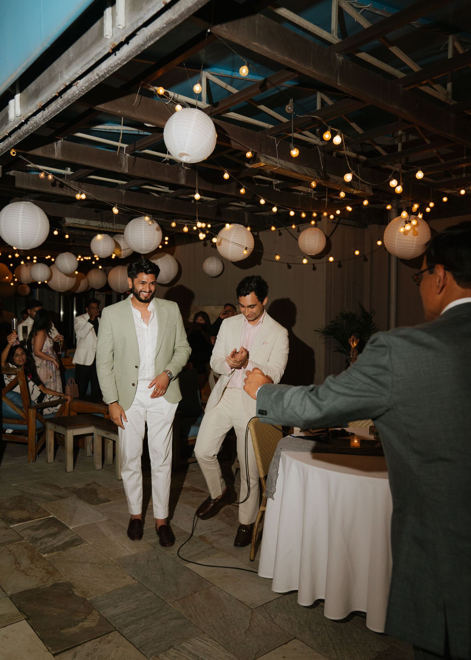 Wedding guests dance in a venue decorated with white paper lanterns and string lights.