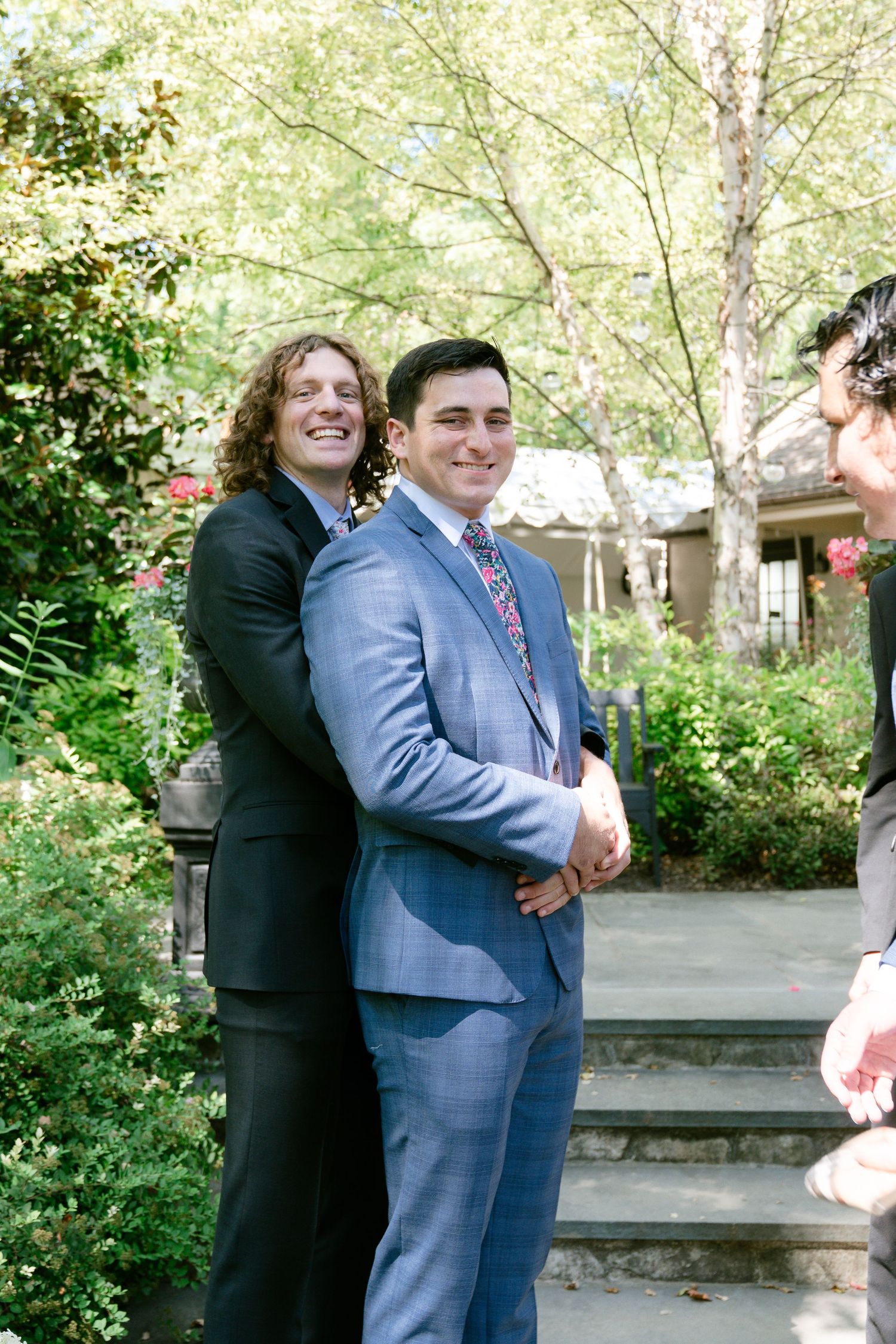 A couple shares a joyful embrace in an outdoor garden setting wearing formal attire.
