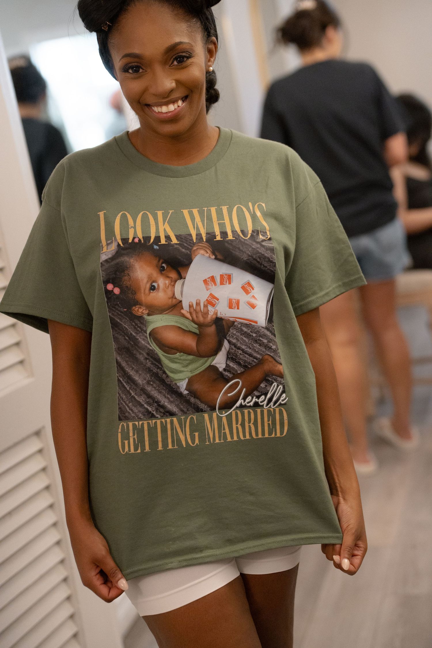 Woman smiling in olive green t-shirt reading Look Who's Getting Married Chevelle with baby photo print.