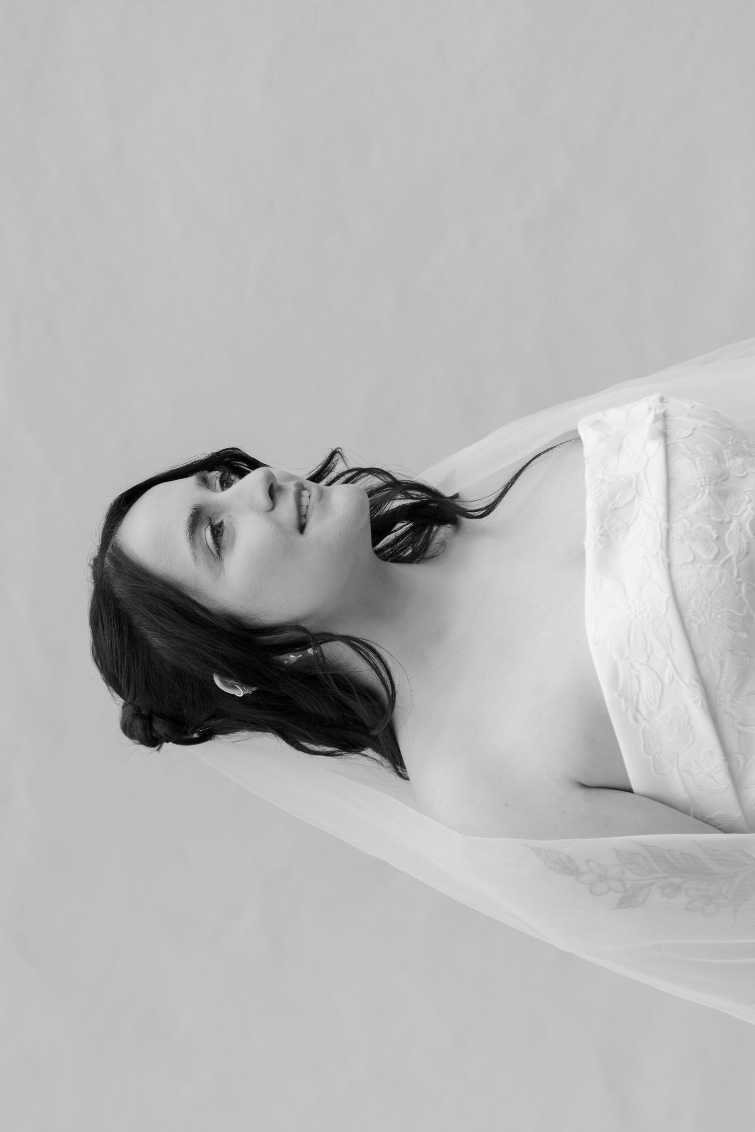Black and white portrait of a woman with dark hair wearing a white strapless top, head tilted back gracefully.