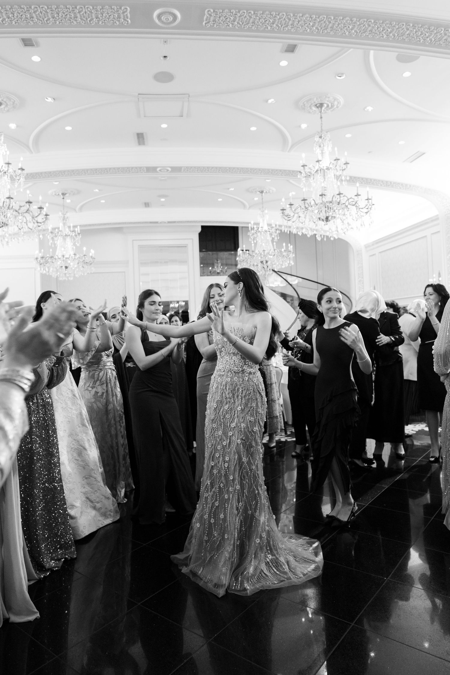 People dancing and celebrating at an elegant ballroom reception with sparkling chandeliers and formal attire.
