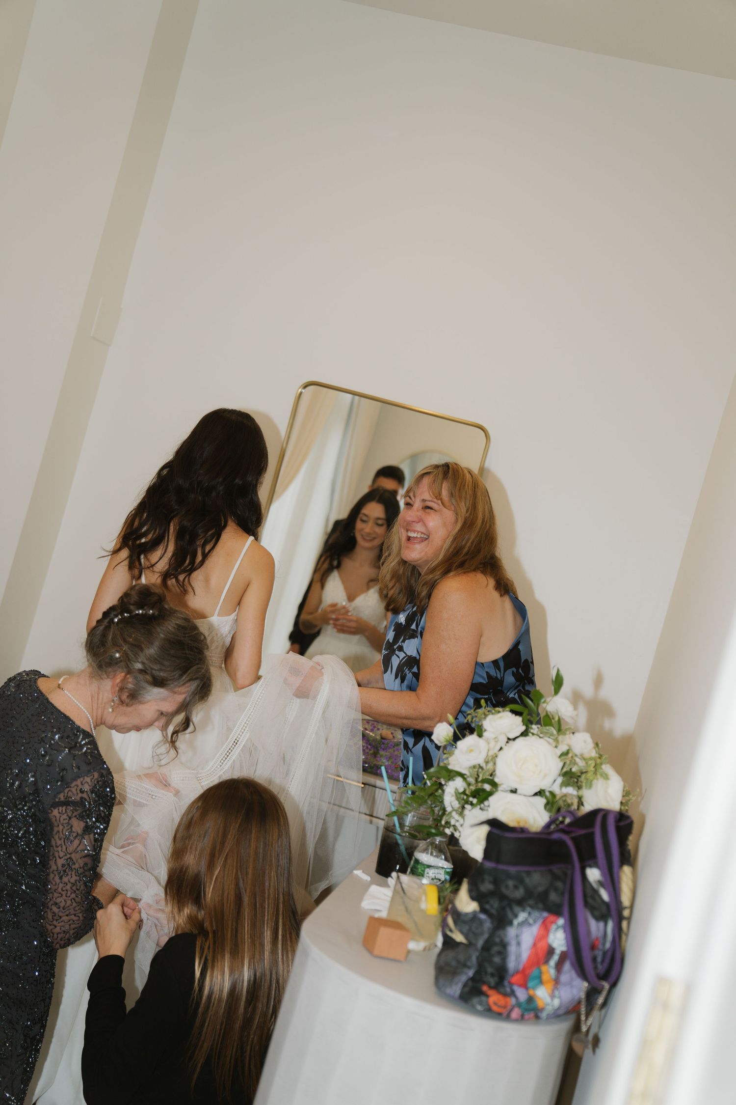A group of wedding guests sharing emotional embraces and celebrating in a bright indoor venue with white walls.