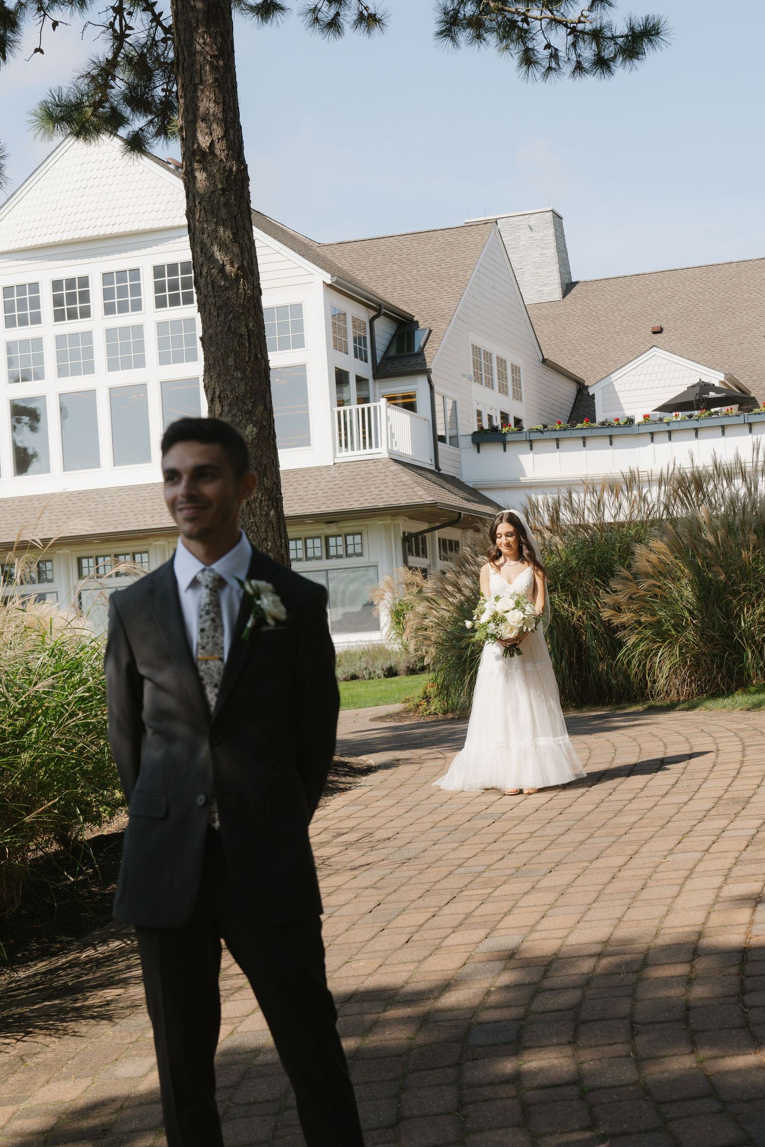 A wedding scene captured at a coastal venue with brick pathways and white buildings in the background.