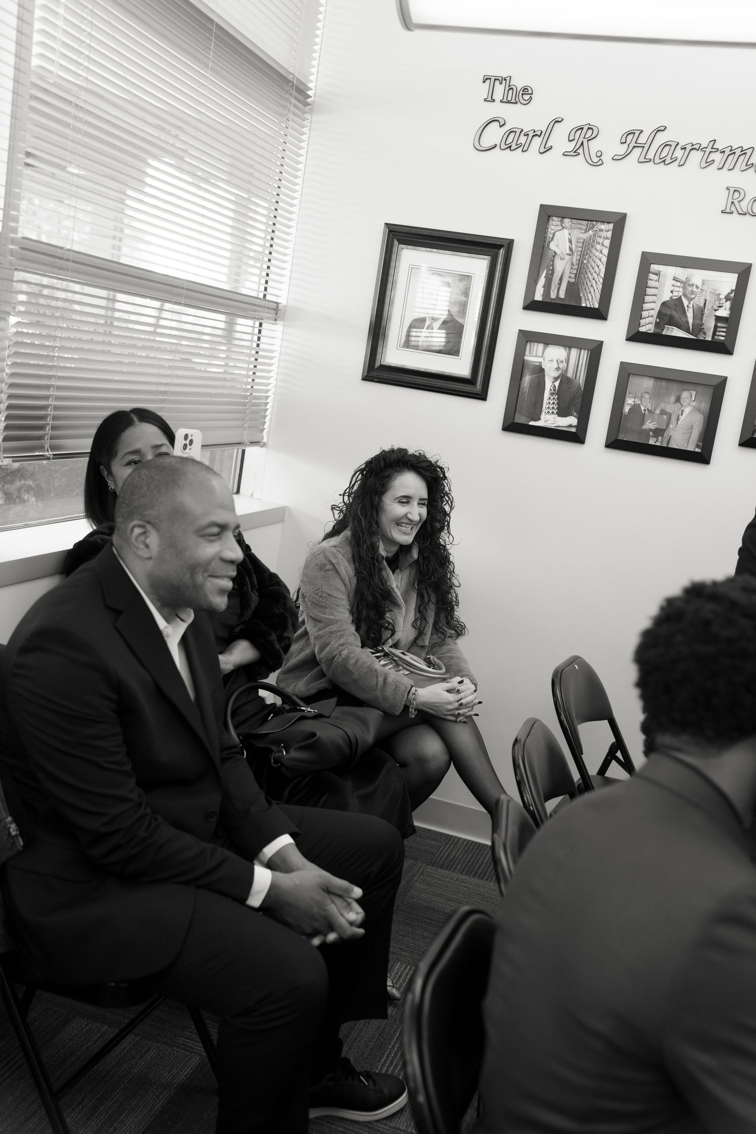 People laughing together during a casual meeting in an office with photos and blinds in background.