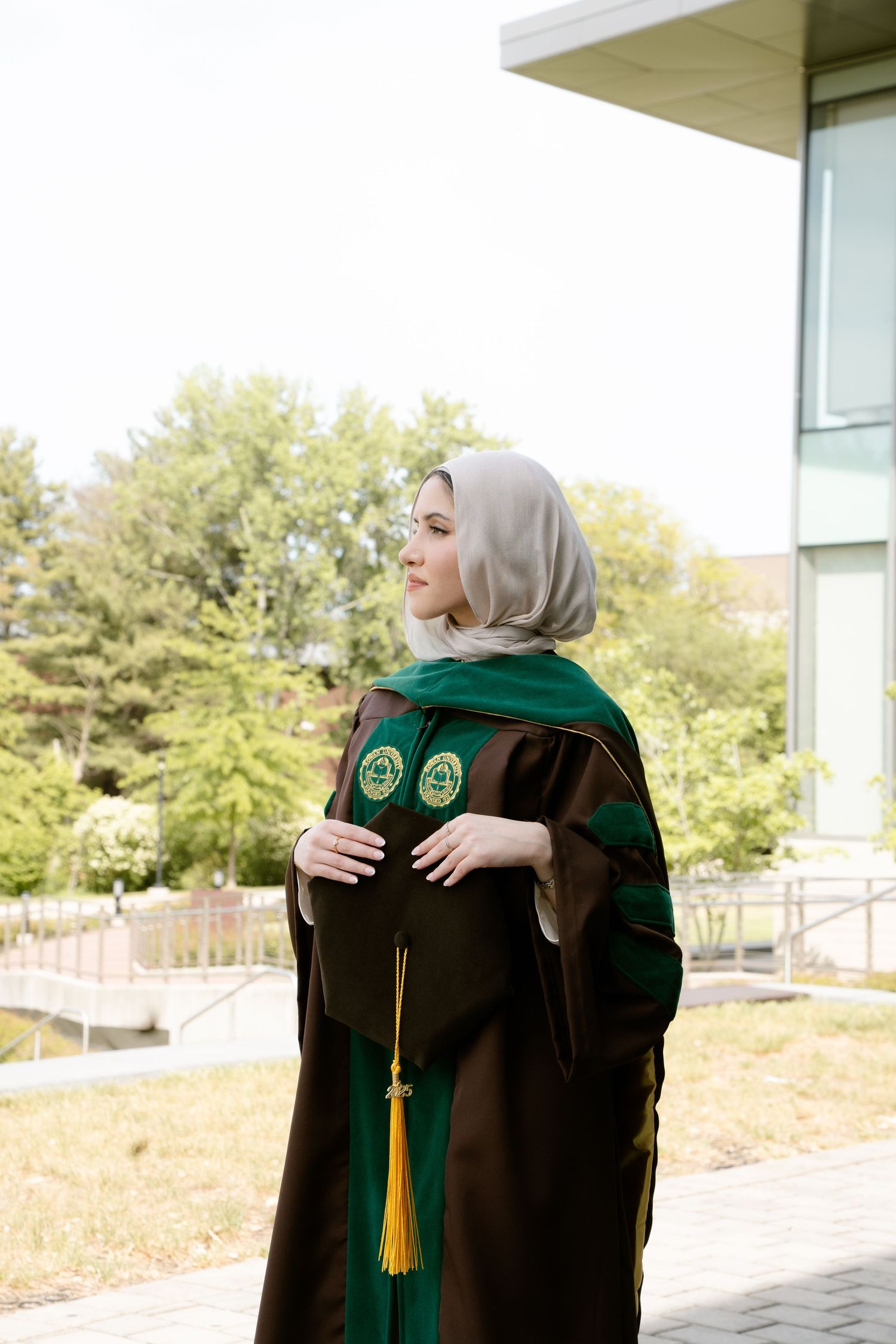 Graduate in academic regalia with green and brown robes standing outdoors.