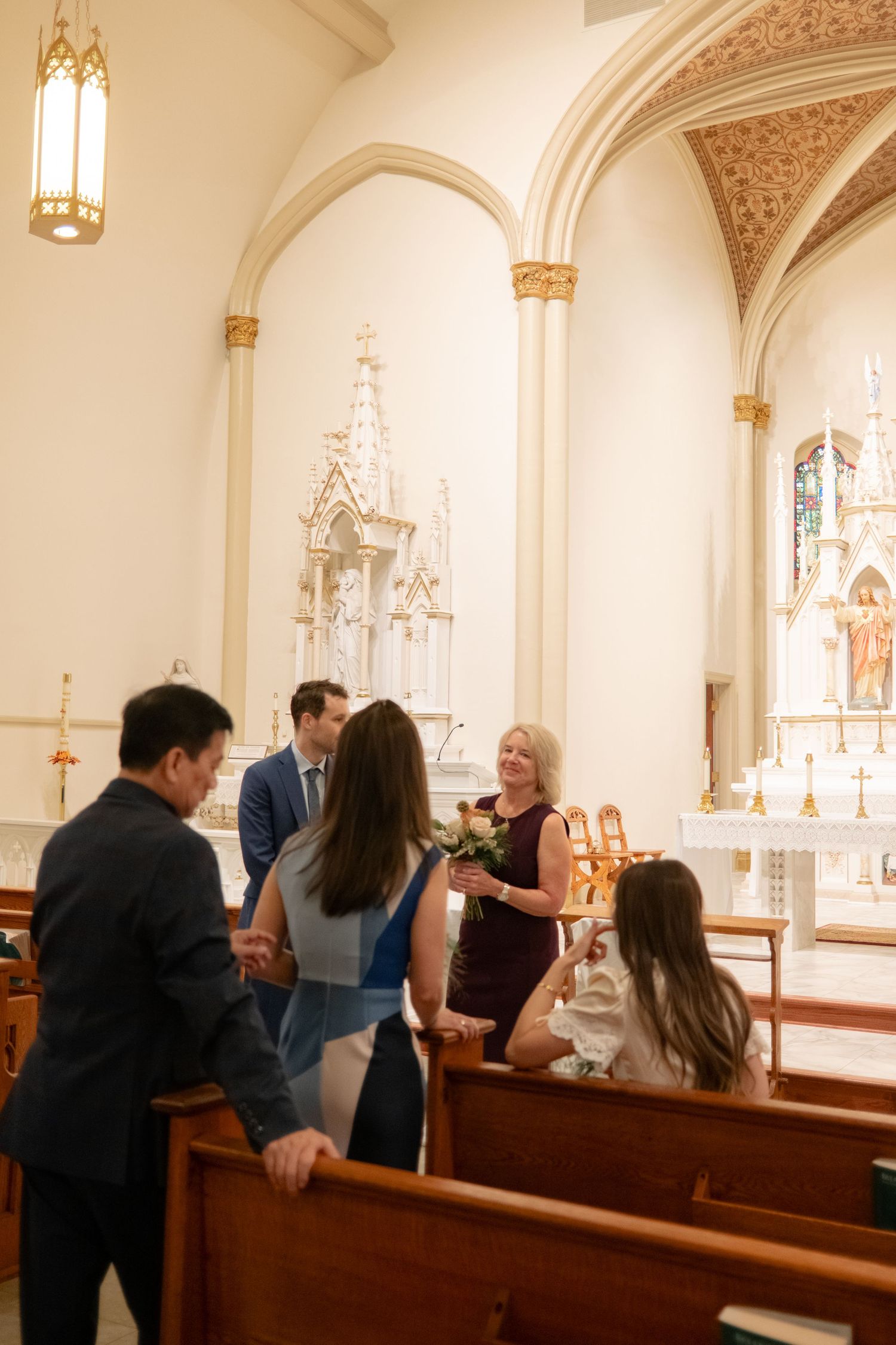 Wedding guests gather inside an ornate church with Gothic architectural details and stained glass windows.