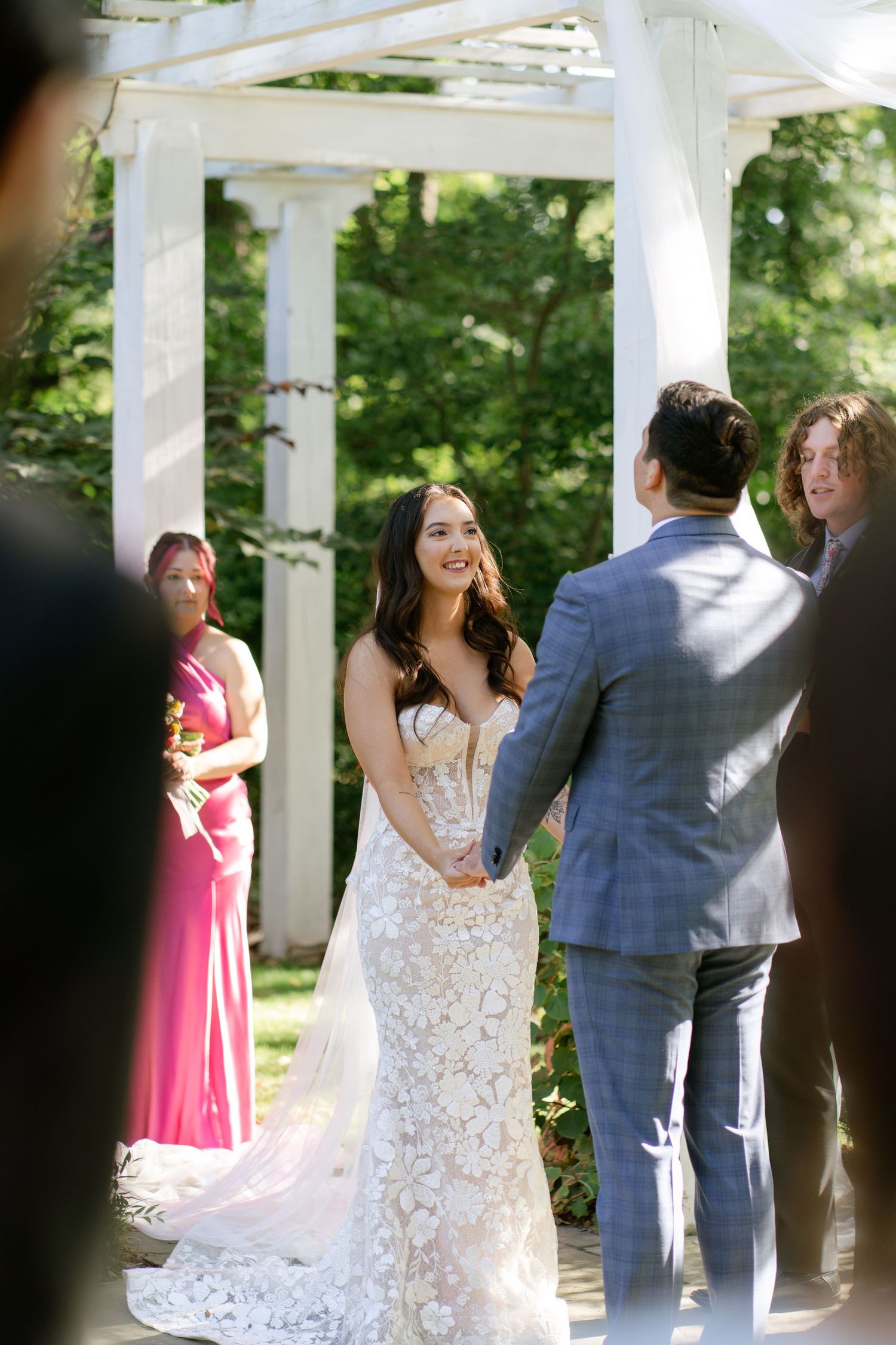 Wedding ceremony moments under a white pergola with guests in formal attire.