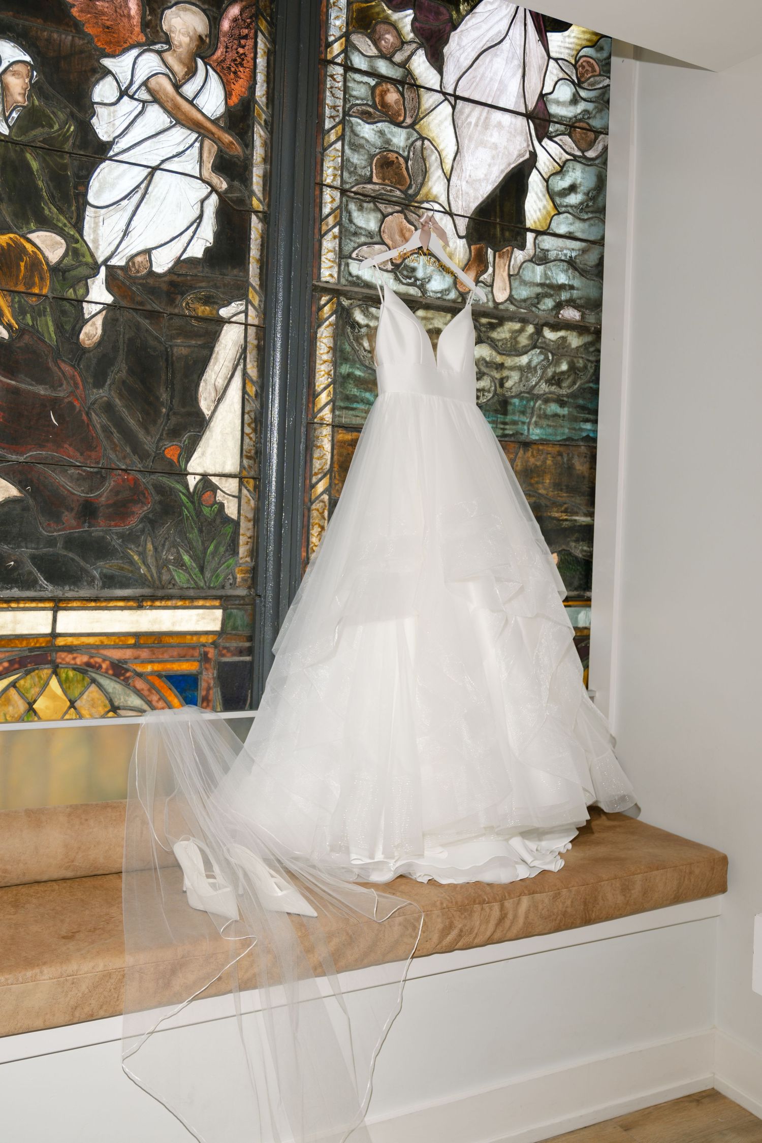 Stunning white wedding gown displayed on bench against decorative stained glass window background.