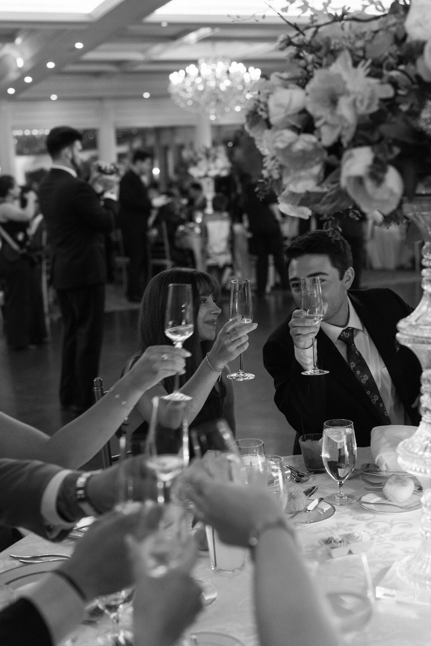 Guests raising champagne glasses in a toast at an elegant wedding reception in black and white photo.