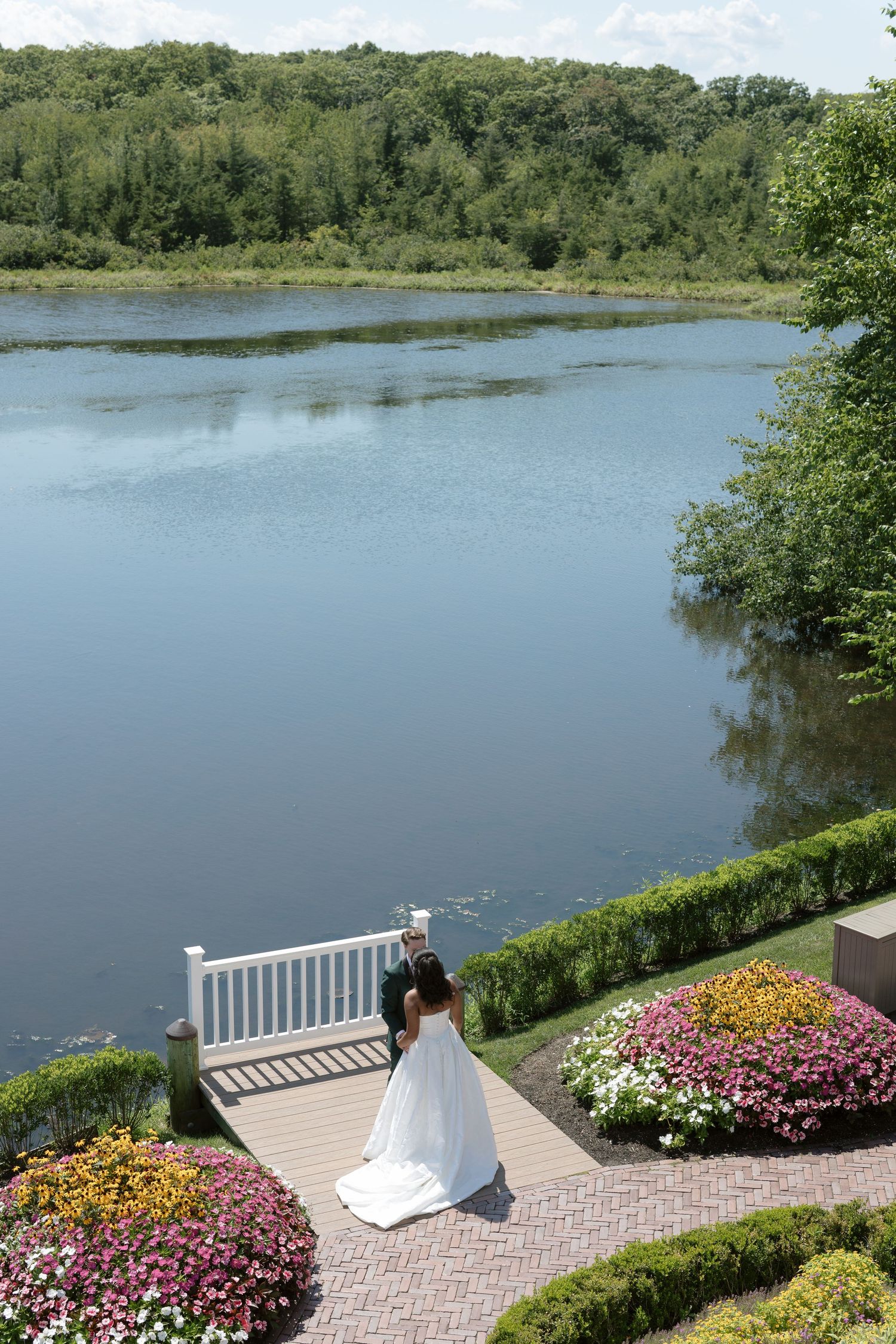 Bride and groom share a romantic moment on a lakeside deck surrounded by colorful flowers.