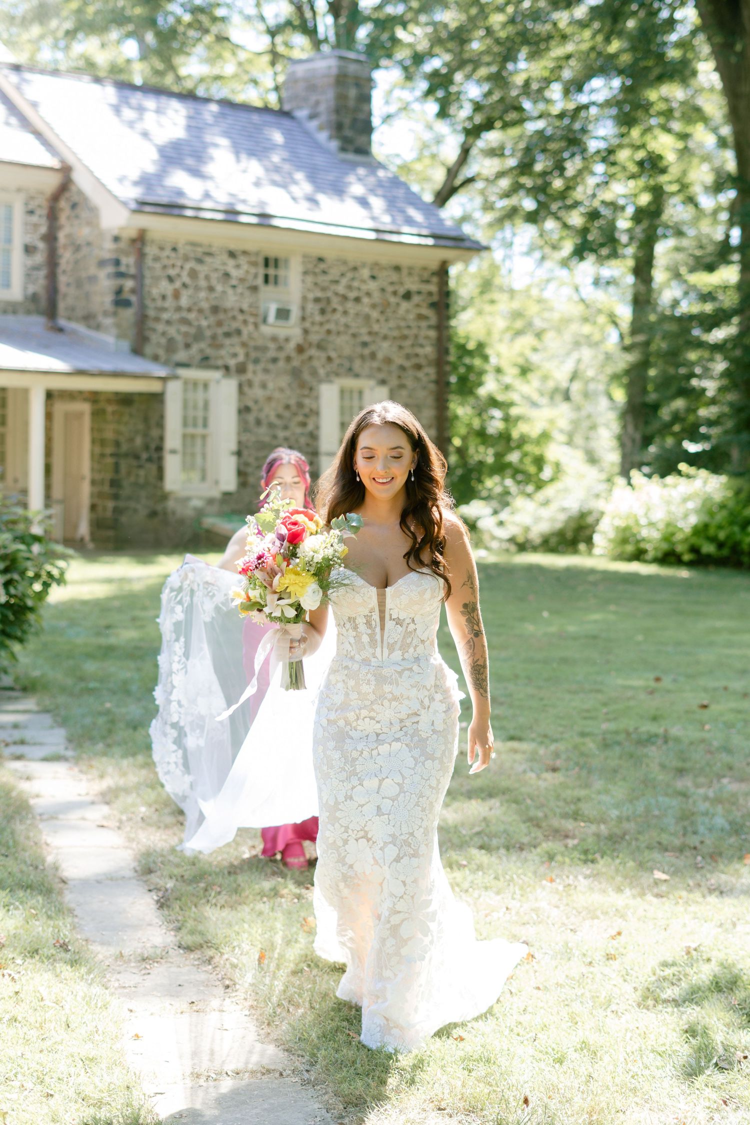 A person in a white lace wedding dress twirls joyfully in a sunlit garden setting with stone buildings in the background.