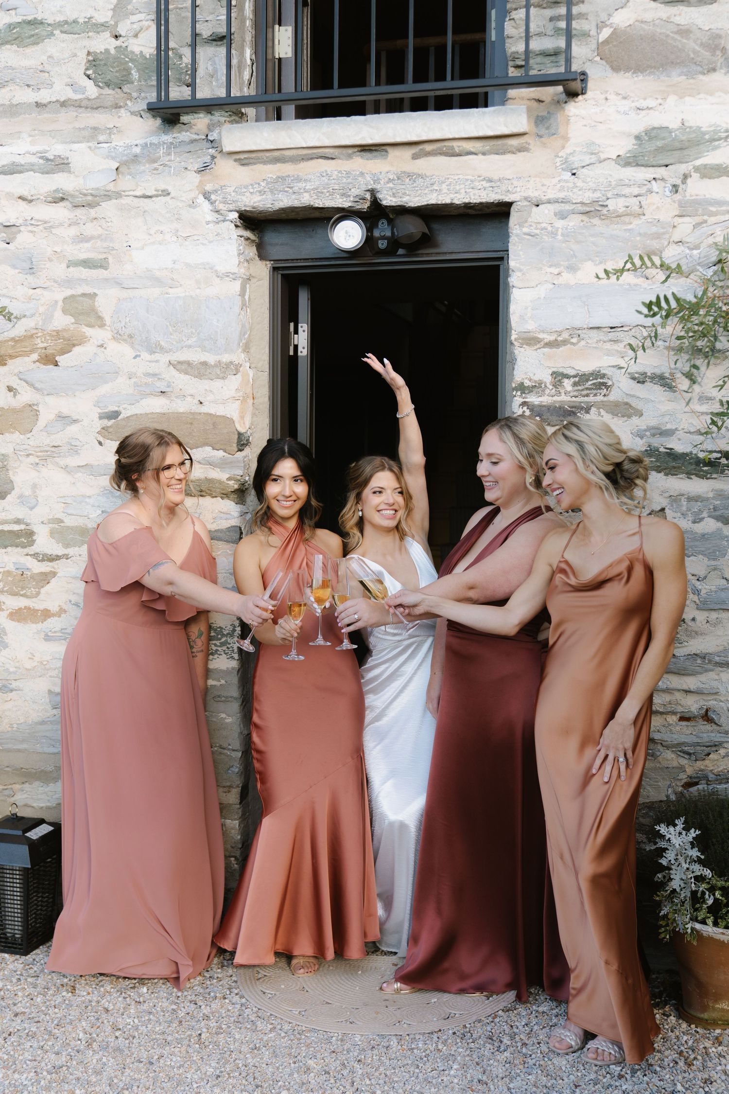 Wedding party in coordinating dusty rose dresses posing against stone wall.