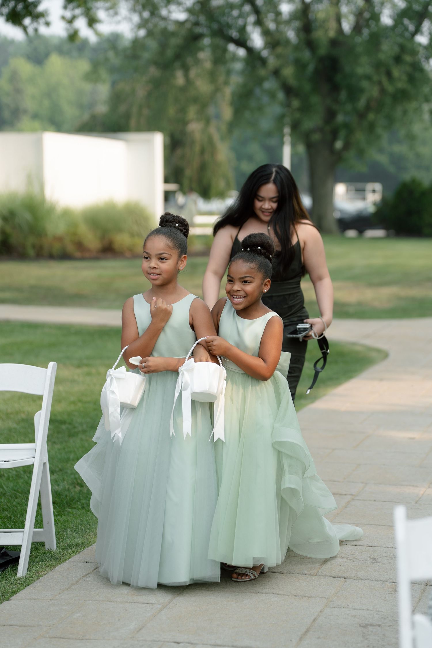 Two young flower girls in mint green dresses carry baskets at outdoor wedding ceremony.
